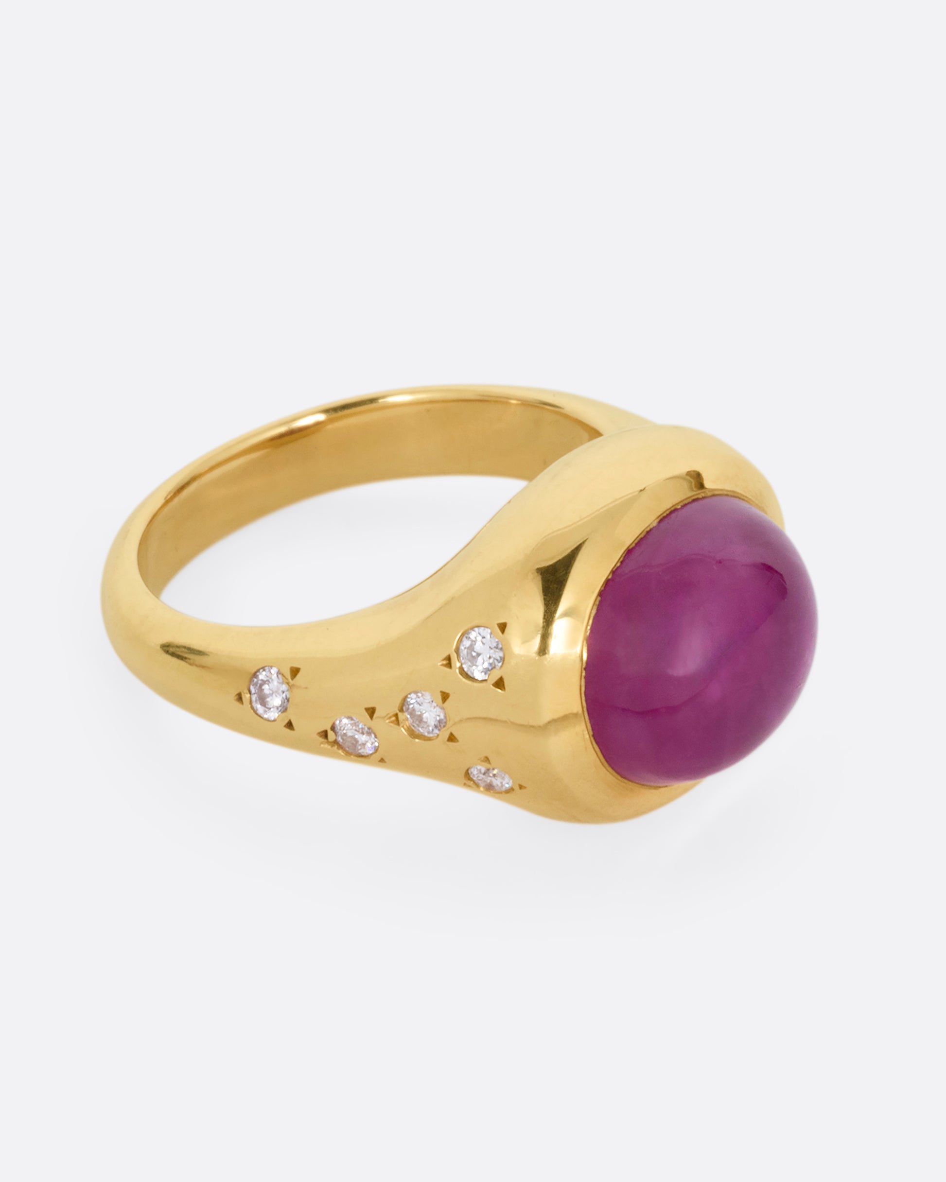A yellow gold signet ring with a ruby cabochon and diamonds on either shoulder. Shown from the side.