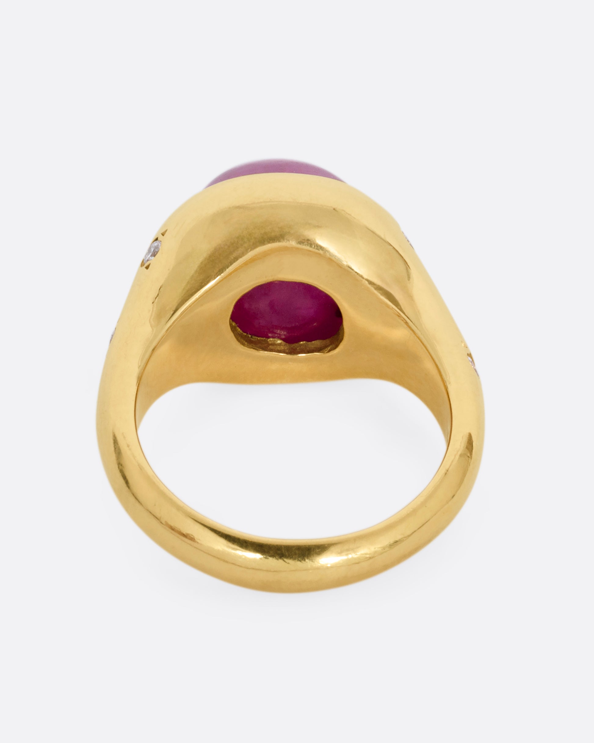 A yellow gold signet ring with a ruby cabochon and diamonds on either shoulder. Shown from the back.