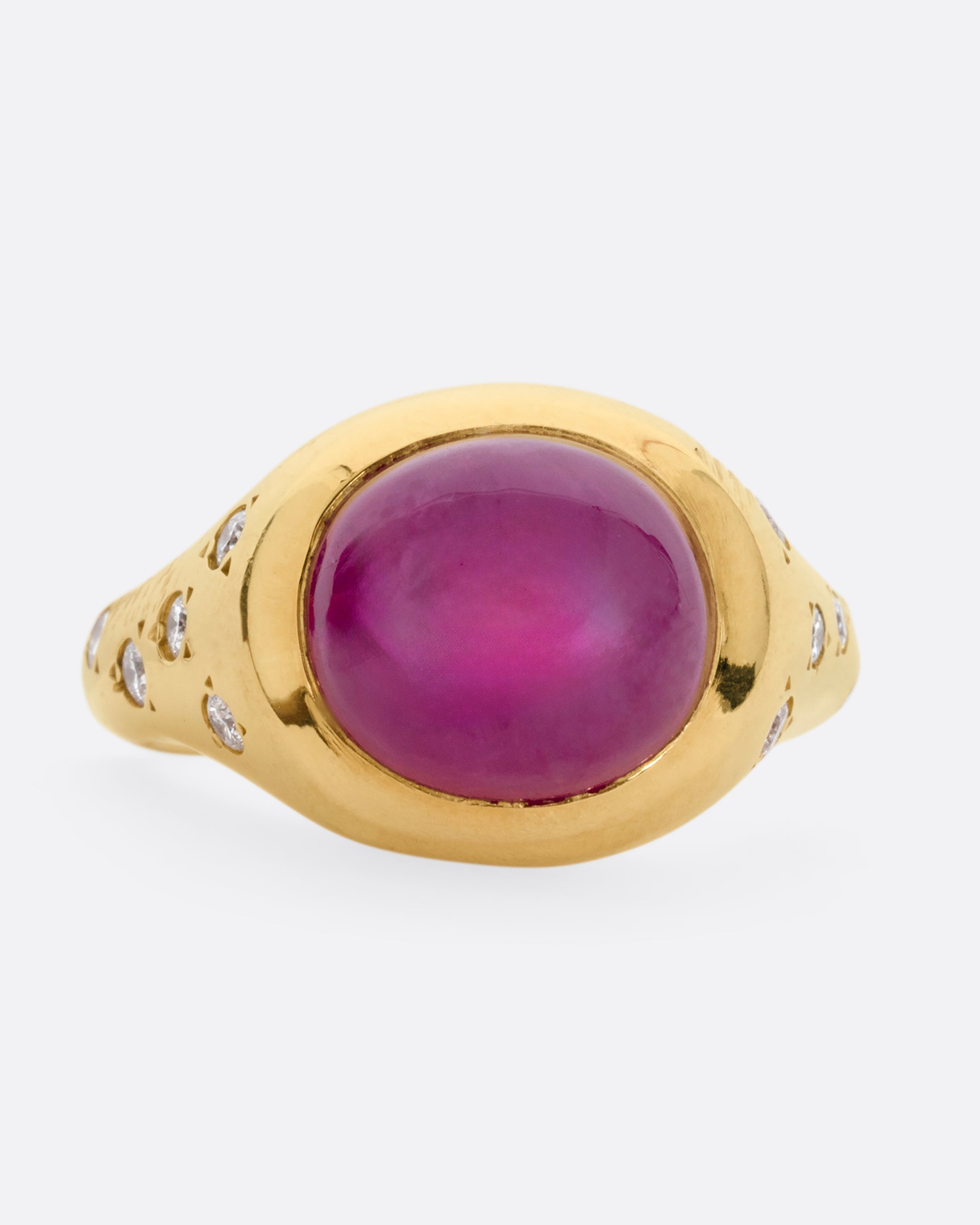 A yellow gold signet ring with a ruby cabochon and diamonds on either shoulder. Shown from the front.