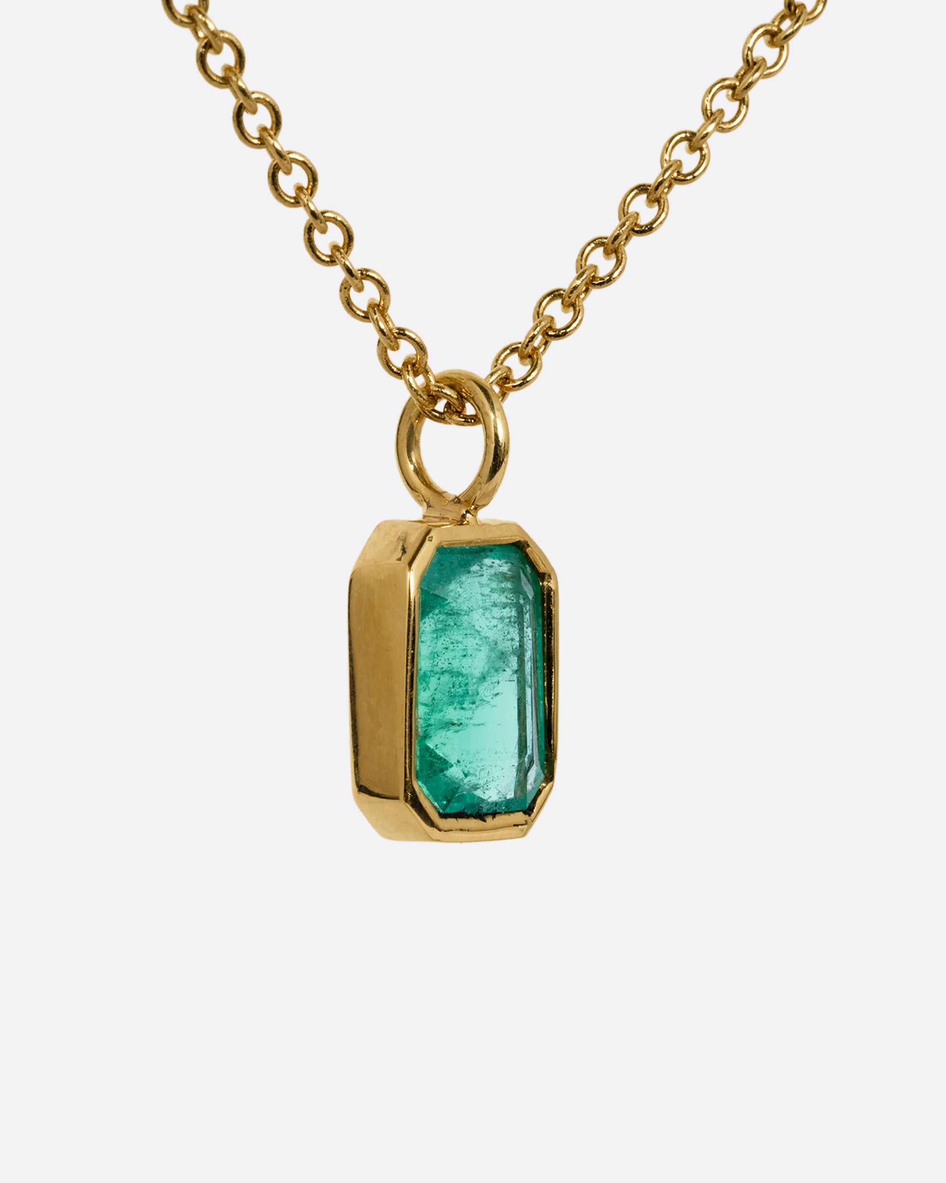 A yellow gold cable chain necklace with a bezel set Zambian emerald. Shown from the side.