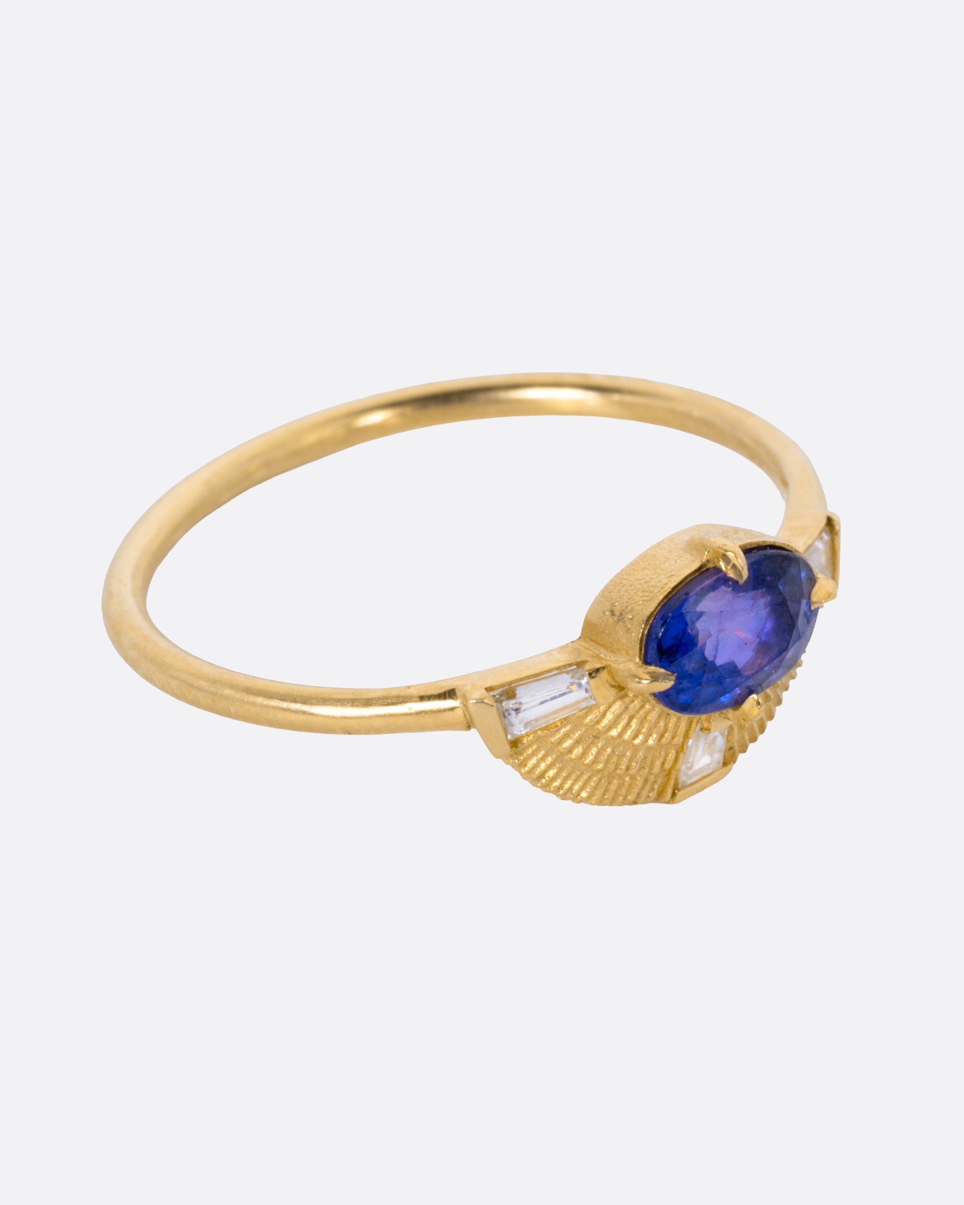 A yellow gold ring with a purple sapphire and three baguette diamonds, shown from the side.