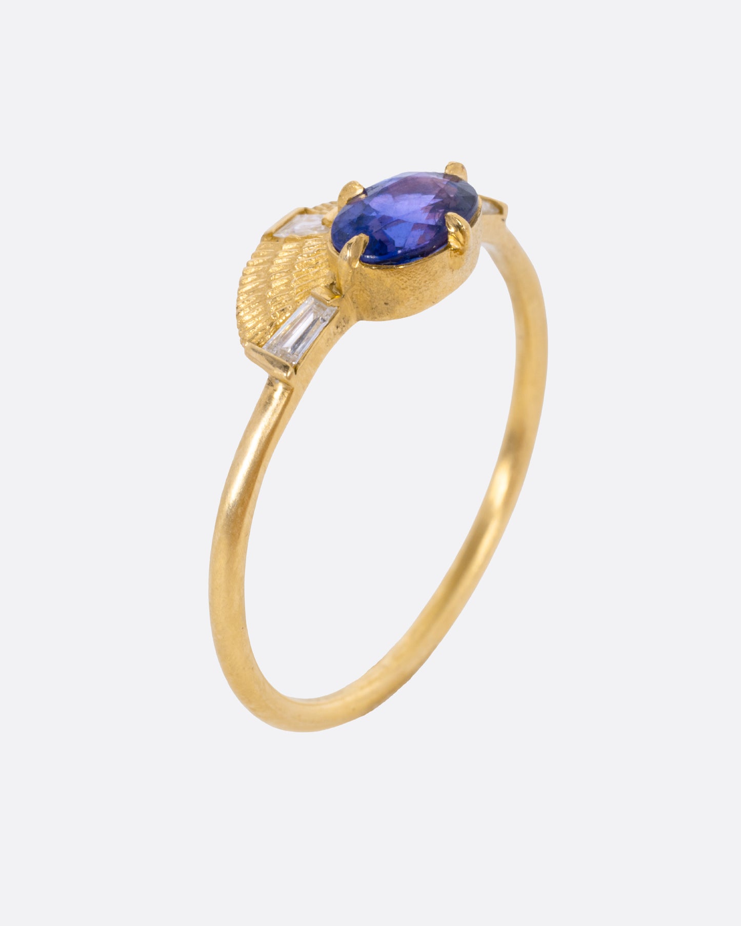 A yellow gold ring with a purple sapphire and three baguette diamonds, shown from the side standing up.