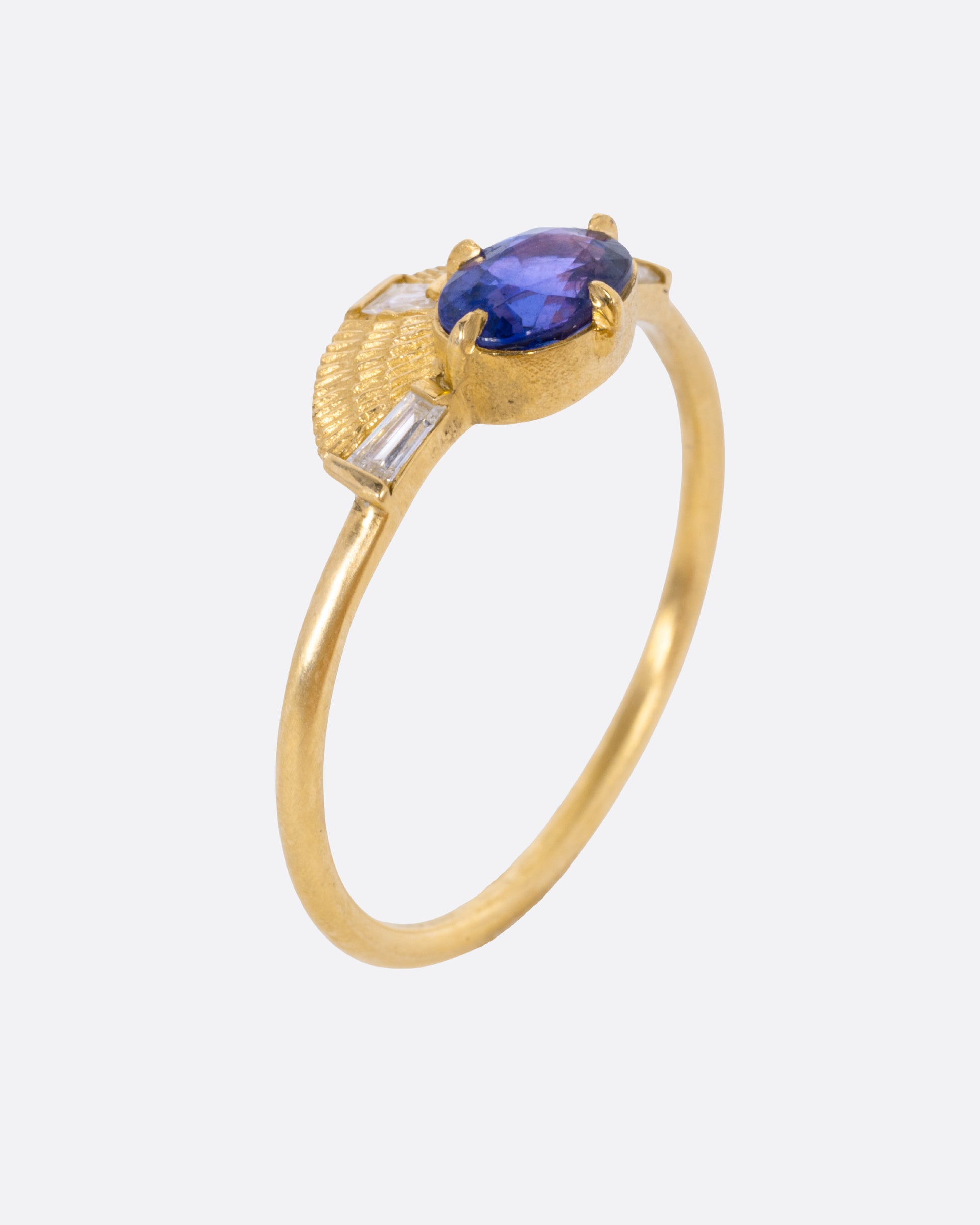 A yellow gold ring with a purple sapphire and three baguette diamonds, shown from the side standing up.