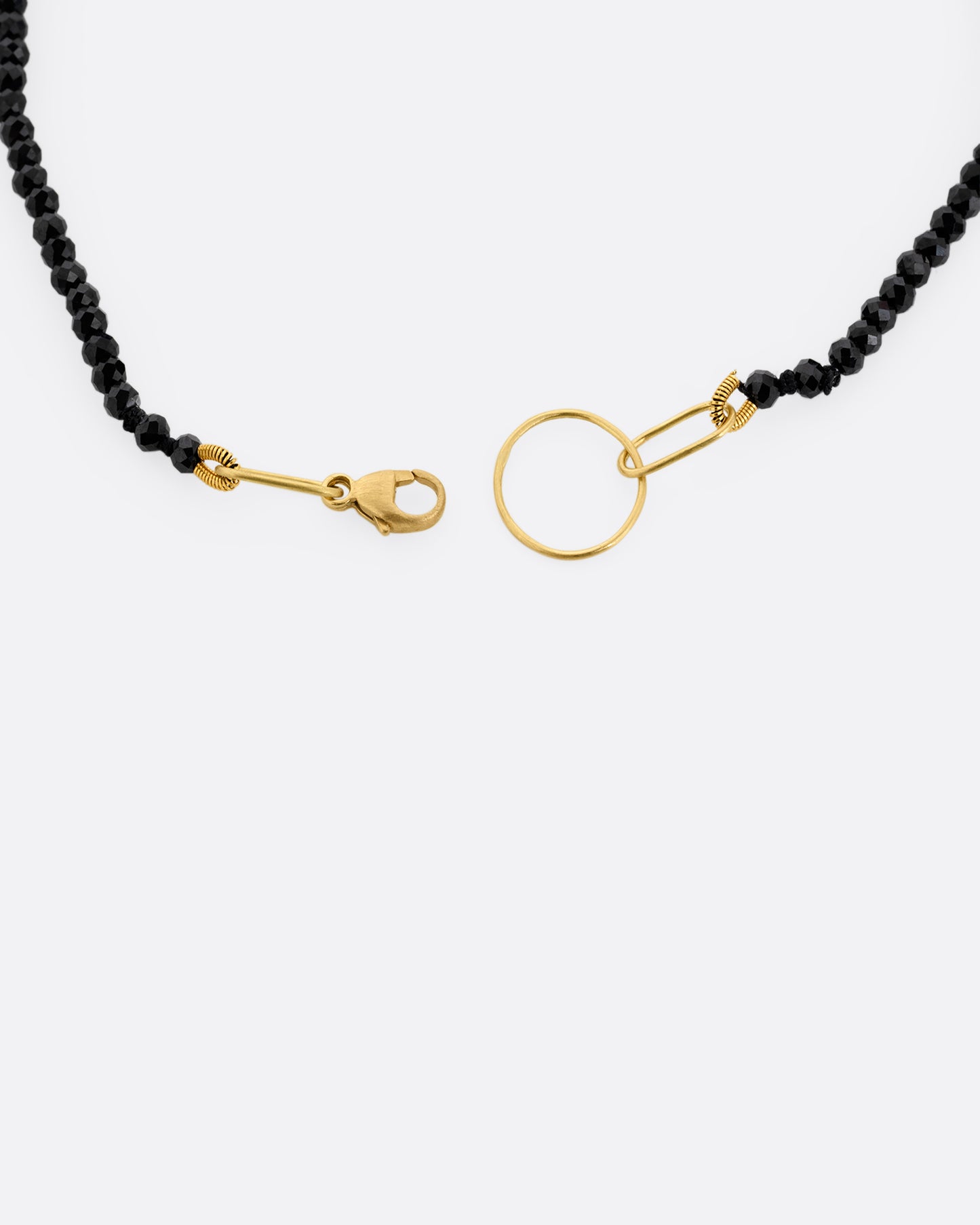 A close up of a black spinel beaded bracelet with a yellow gold clasp. 