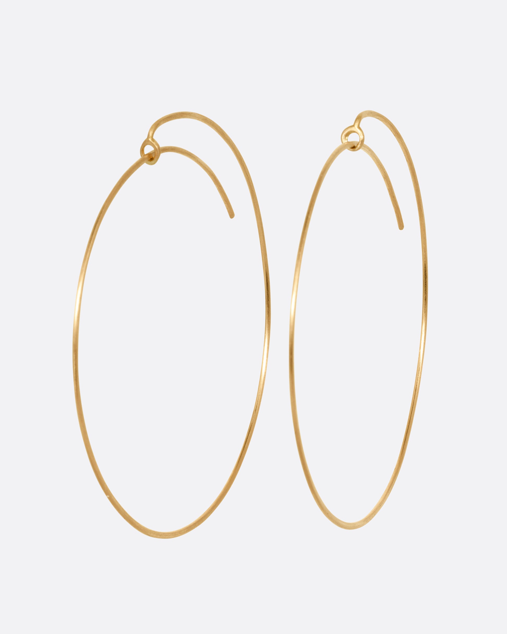 A pair of large yellow gold hoops with a  minimalist wrap-around style top. Shown from the side.