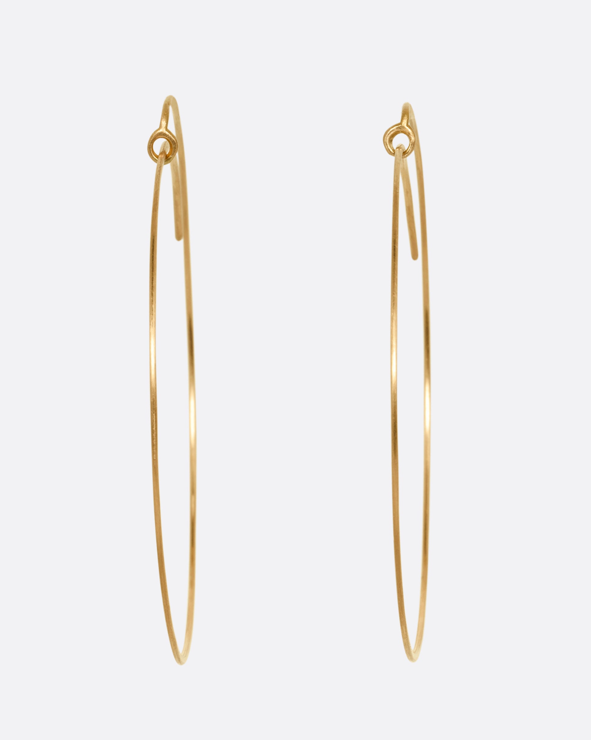 A pair of large yellow gold hoops with a  minimalist wrap-around style top. Shown from the front.