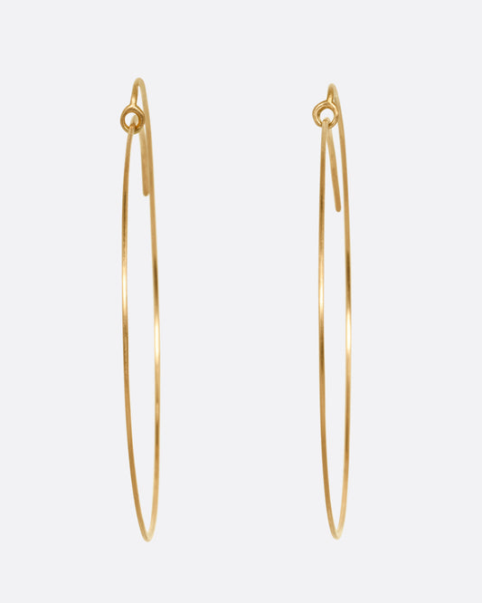 A pair of large yellow gold hoops with a  minimalist wrap-around style top. Shown from the front.