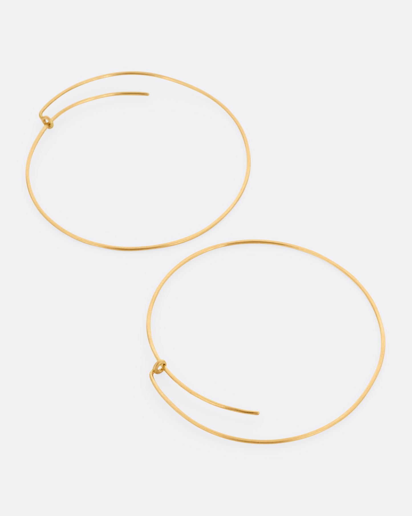 A pair of large yellow gold hoops with a  minimalist wrap-around style top. Shown lying flat from the side.