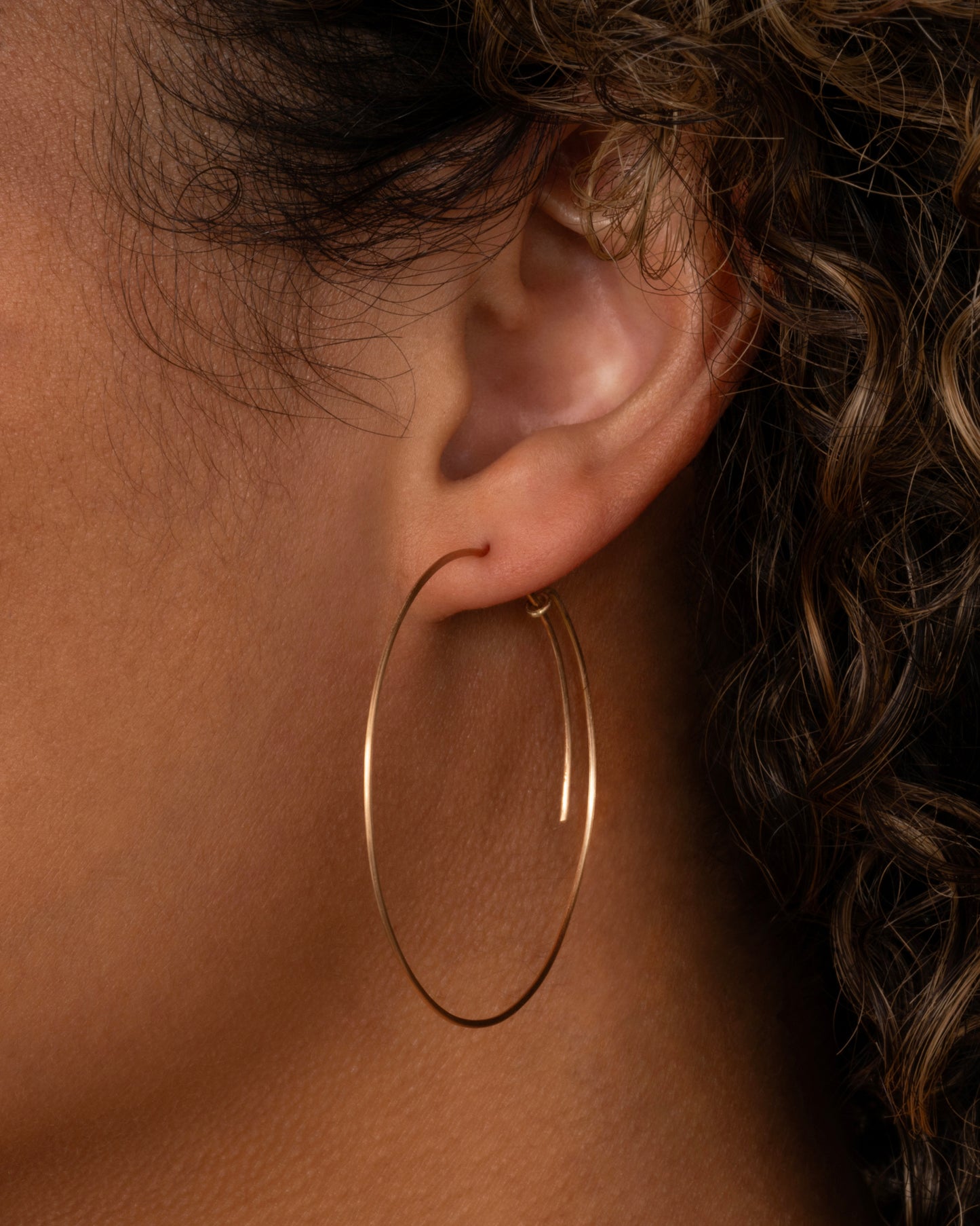 A large yellow gold hoop with a  minimalist wrap-around style top. Shown from the side on a person.