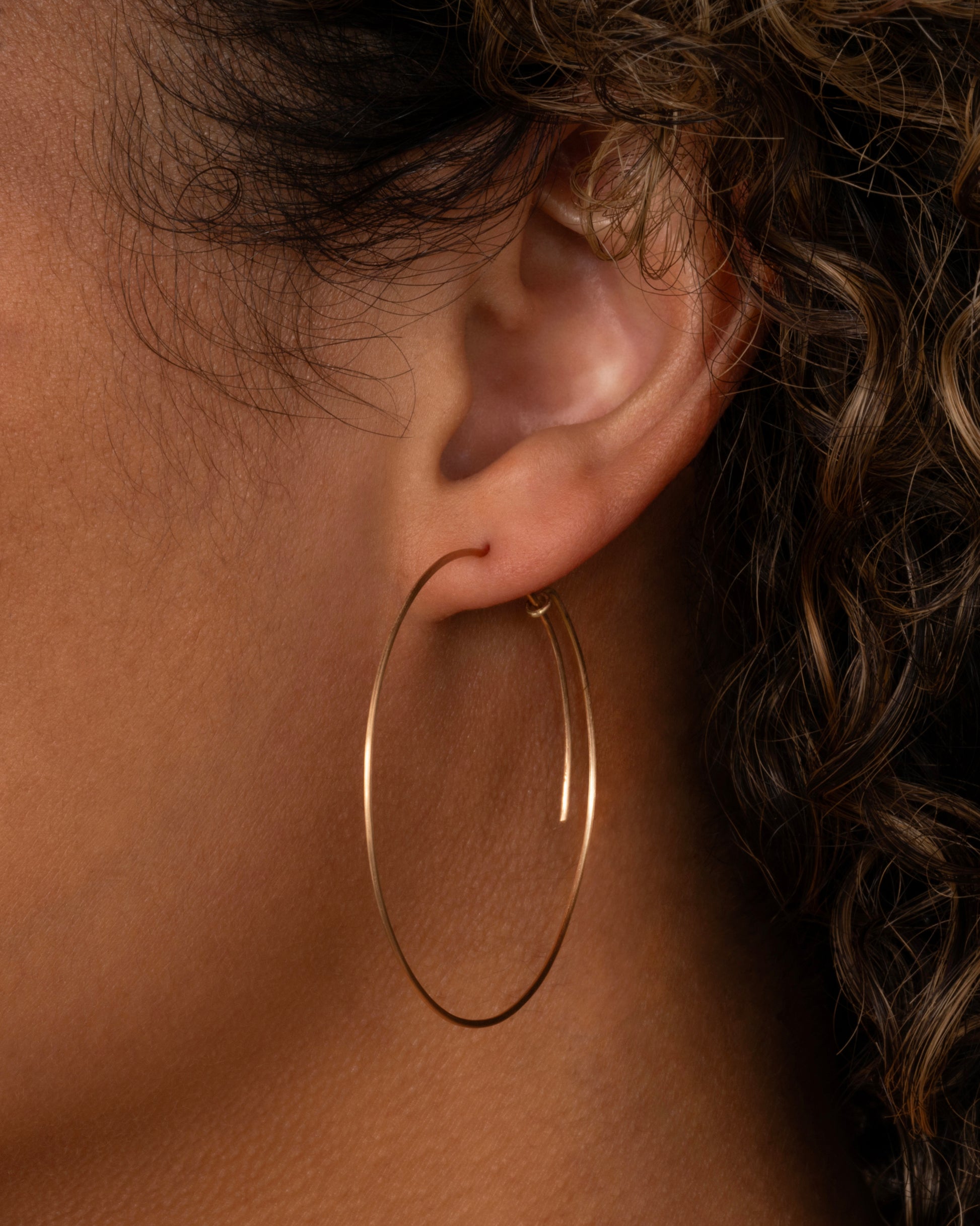A large yellow gold hoop with a  minimalist wrap-around style top. Shown from the side on a person.