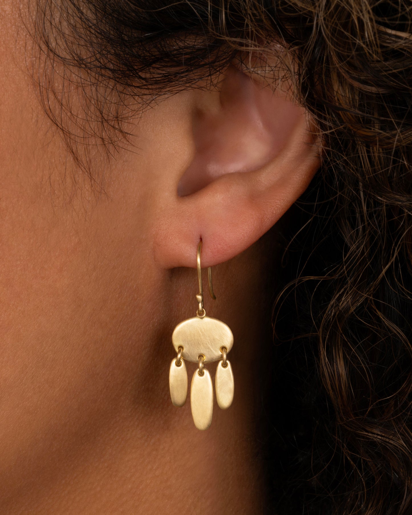 A yellow gold earring with one horizontal oval and  three vertical ovals hanging from links. Shown from the front on a person.
