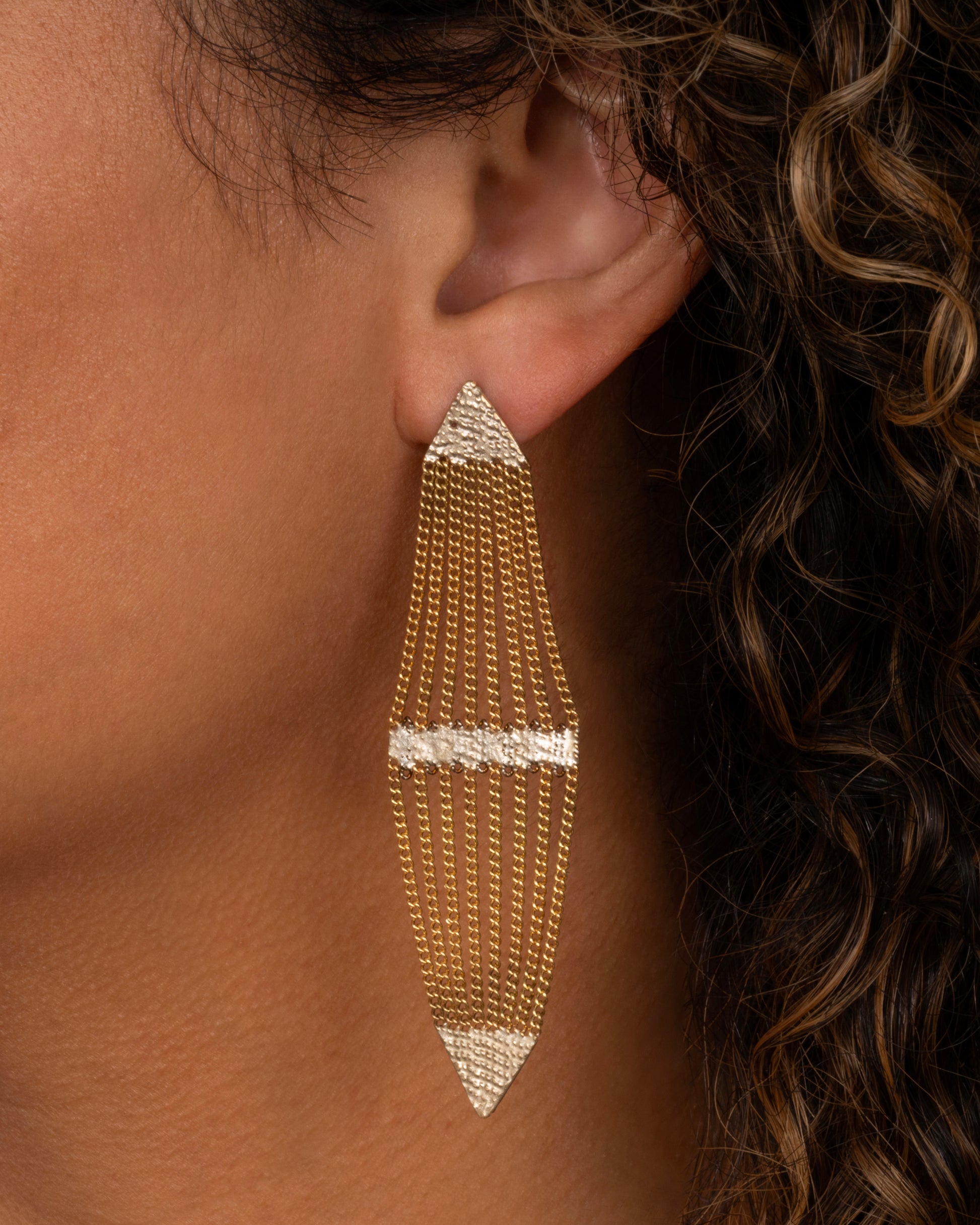 A pair of diamond shaped earrings with silver solder and yellow gold chain. Shown from the front on a person.