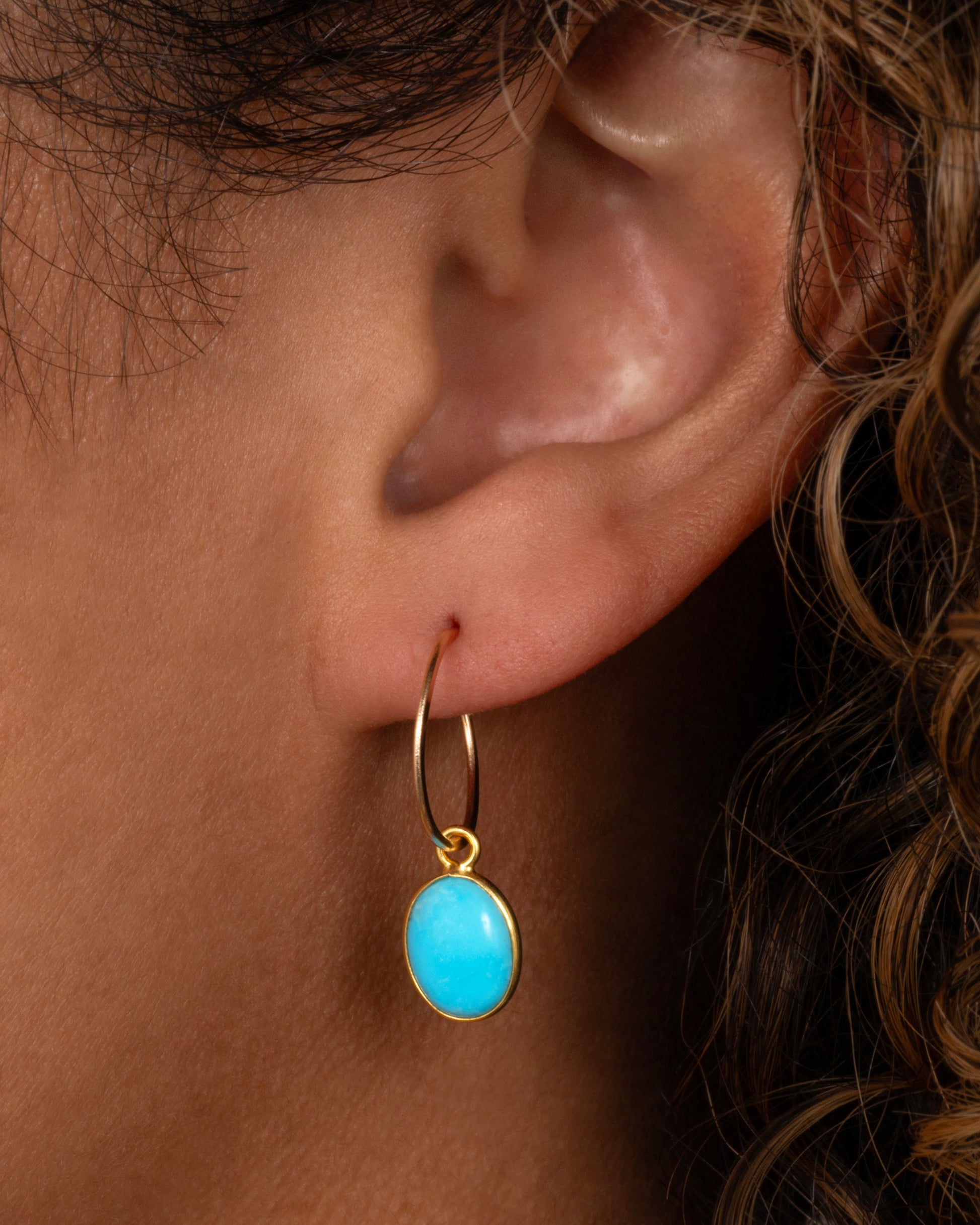 A Sleeping Beauty Turquoise dangle set in yellow gold with a yellow gold bail. Shown on a yellow gold hoop from the front on a person.