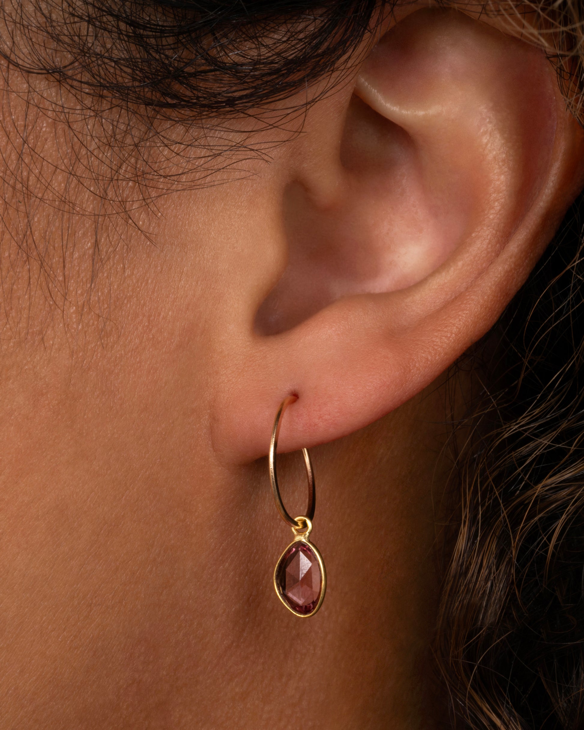 A pink sapphire slice dangle set in yellow gold with a yellow gold bail. Shown on a yellow gold hoop from the front on a person.