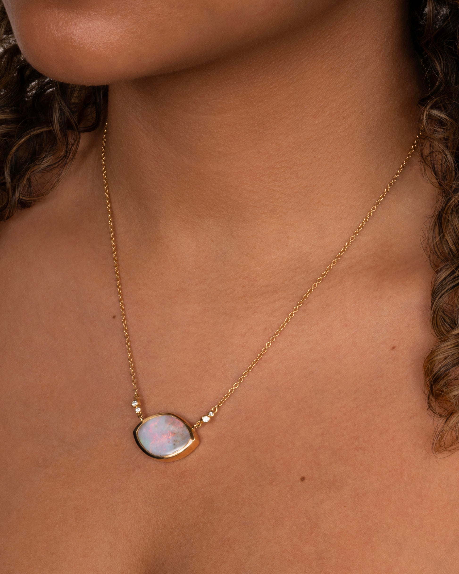 A yellow gold cable chain necklace with a large eye shaped opal pendant and diamond accents. Shown worn around the neck.