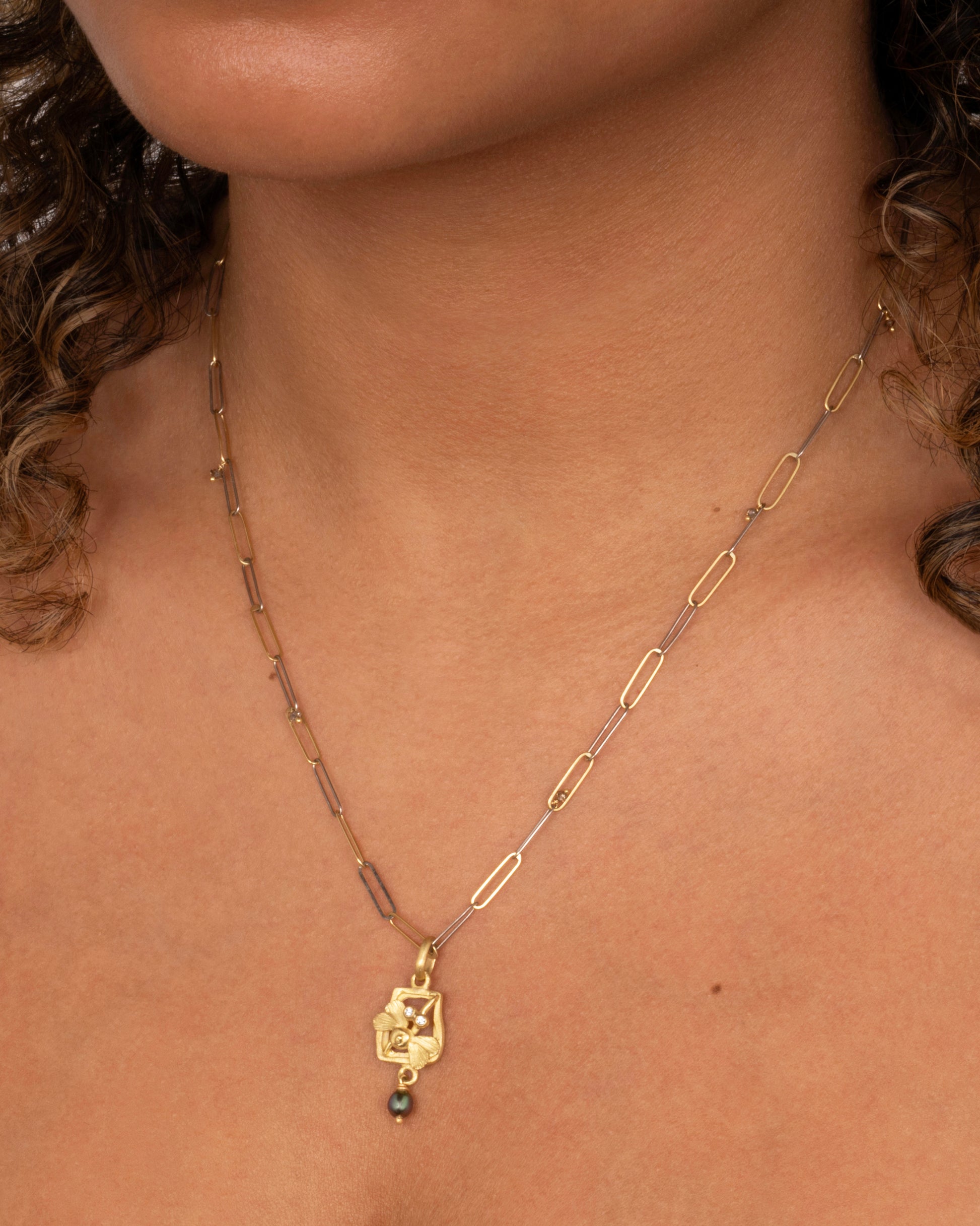 A yellow gold diamond eyed dragonfly charm with a keshi pearl. Shown worn around the neck.