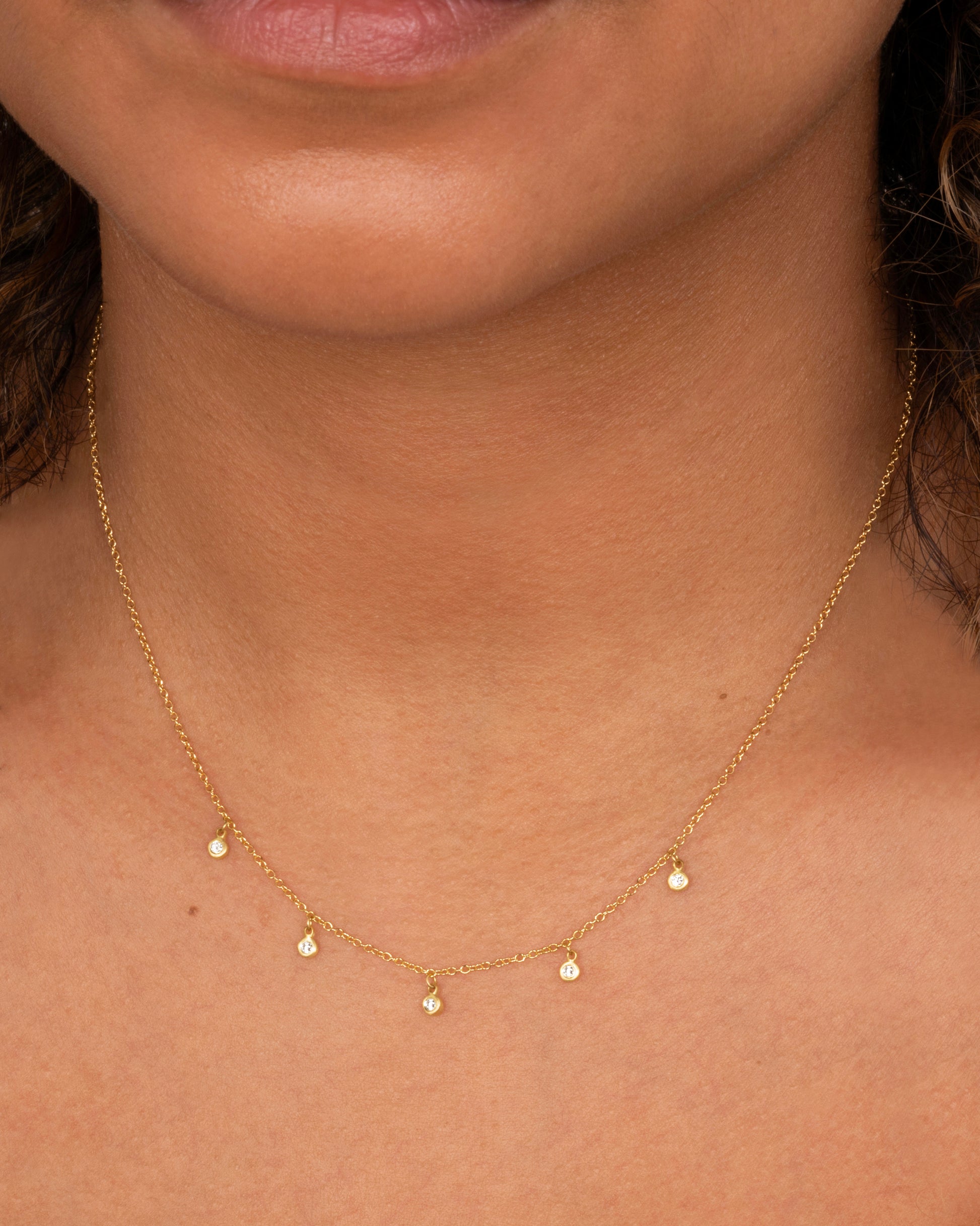 A yellow gold necklace with five brilliant bezel set diamond charms on a cable chain. Shown worn around the neck.