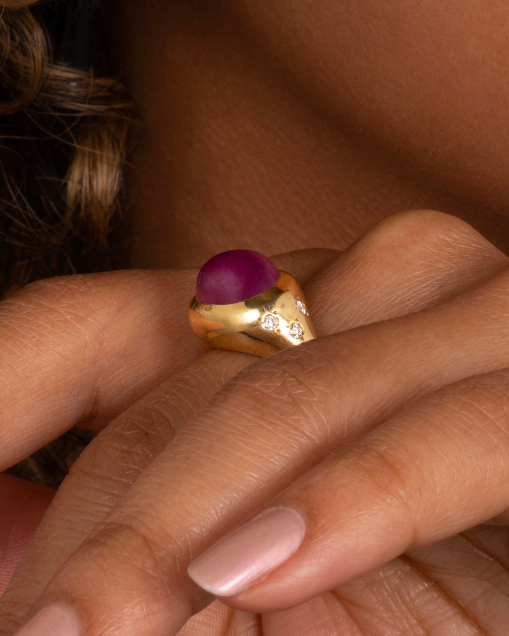 A yellow gold signet ring with a ruby cabochon and diamonds on either shoulder. Shown from the side ob a person.