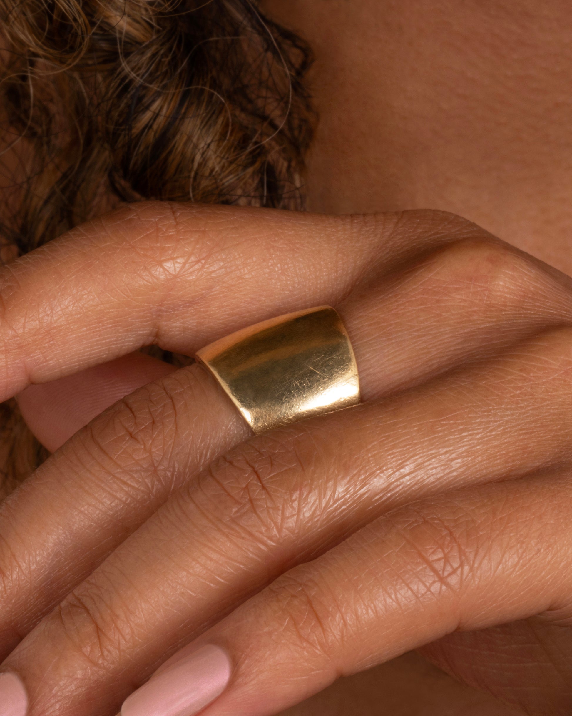 A wide yellow gold band. Shown worn on a hand.