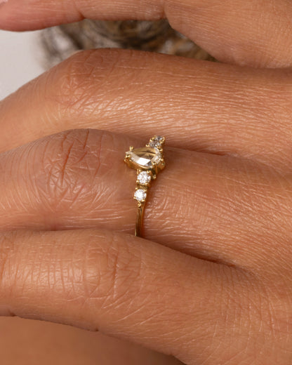  A yellow gold ring with a pear shaped champagne diamond with round white diamond accents. Shown on a hand.