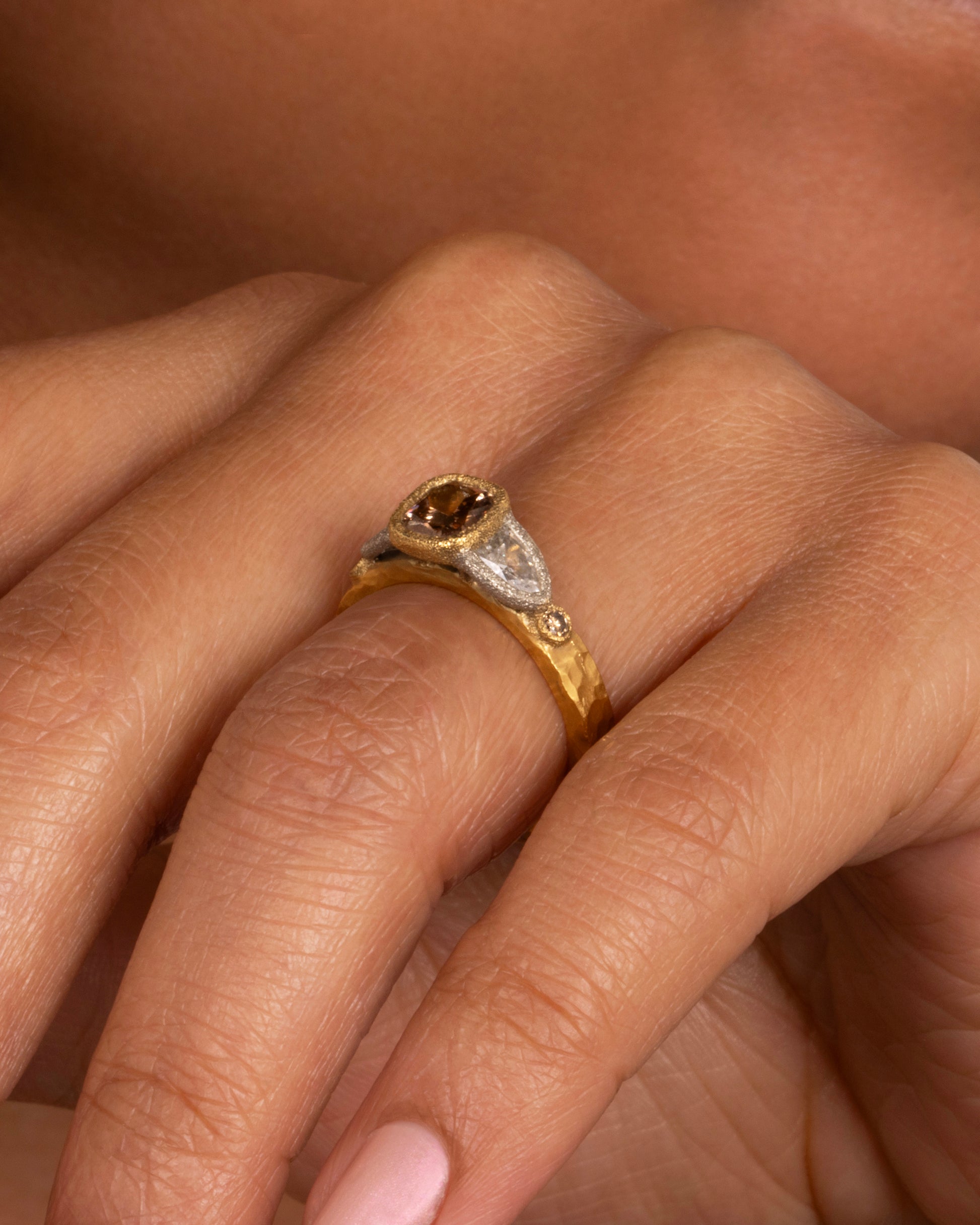 A yellow gold ring with a cushion cut cognac diamond at the center flanked by two shield cut diamonds and two smaller round cognac diamonds. Shown on a hand from the front.