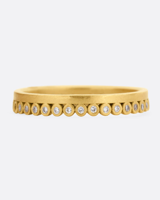 A yellow gold ring with bezel set diamond dots encircling one side. Shown from the front.