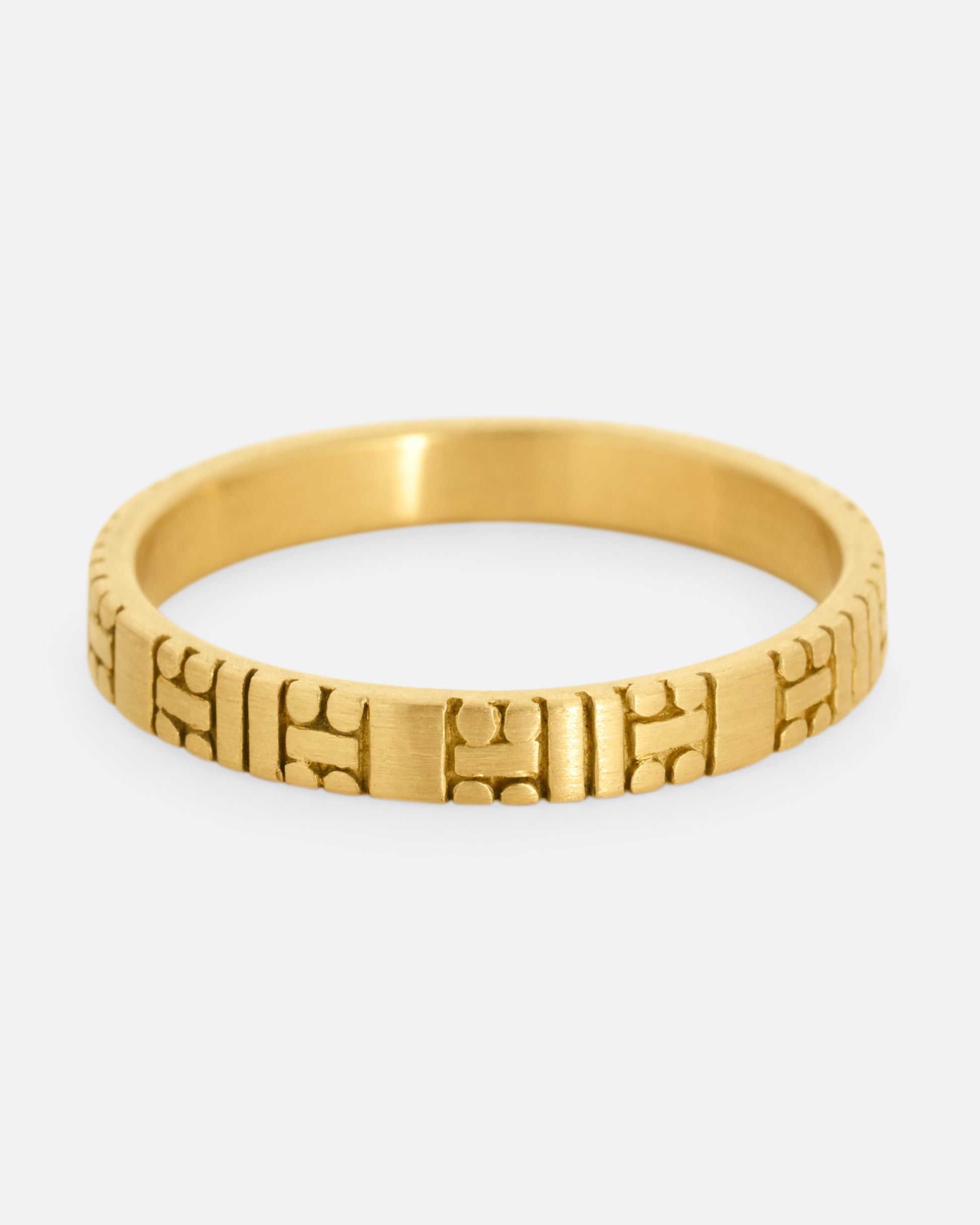 A yellow gold band with dots and dashes in a symmetrical pattern. Shown from the front.