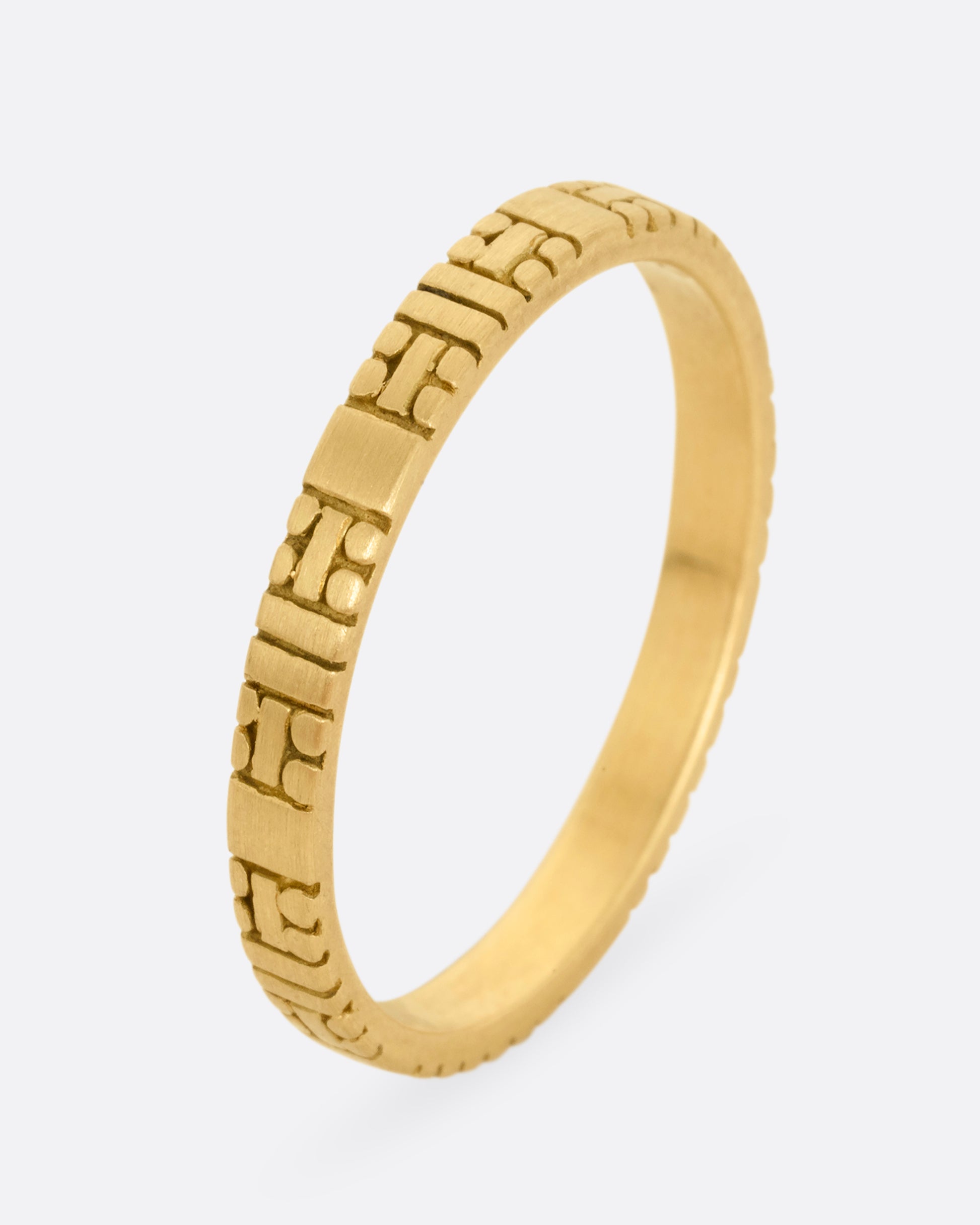 A yellow gold band with dots and dashes in a symmetrical pattern. Shown standing up from the front.
