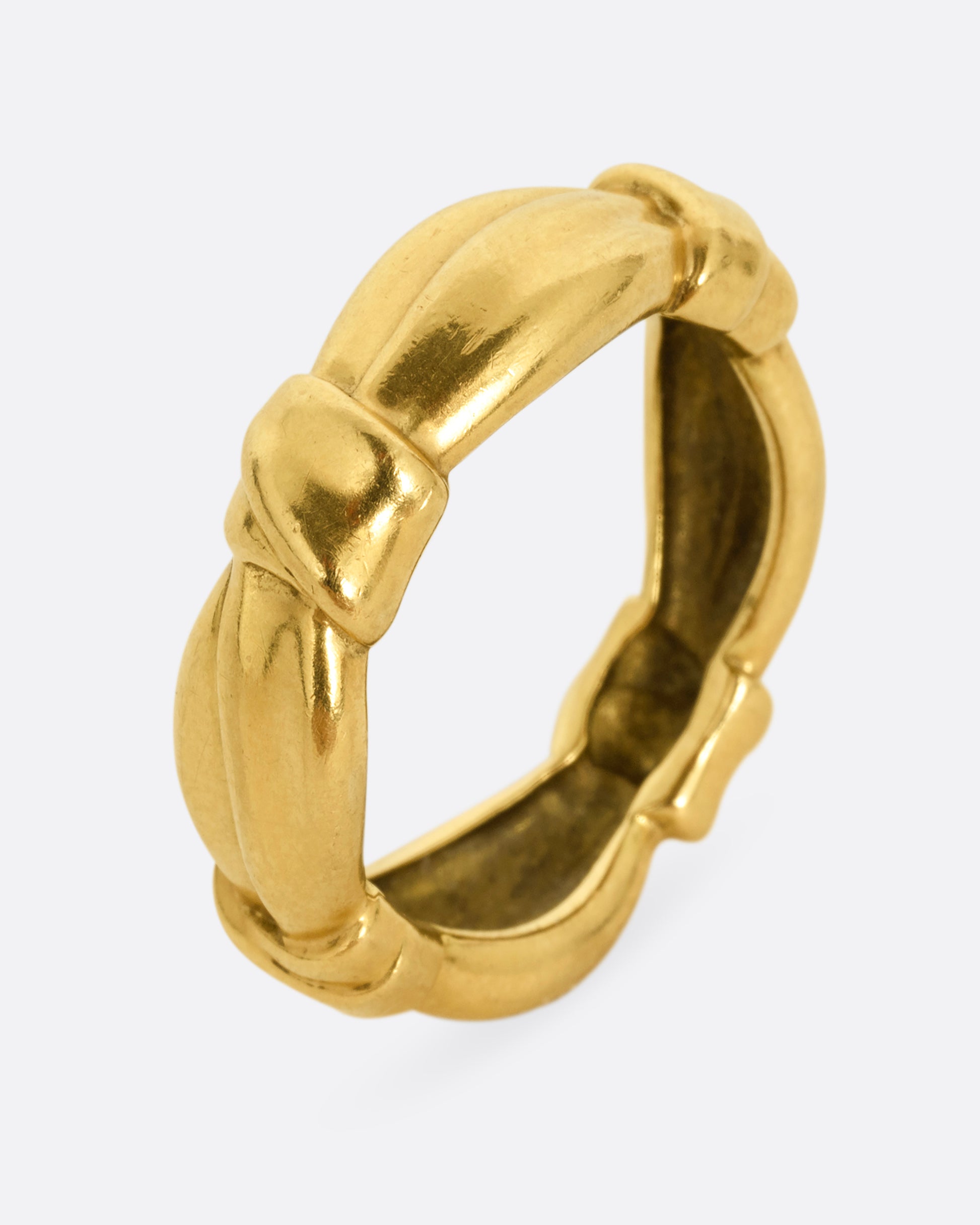A yellow gold ring with bow knots throughout. Shown standing up from the side.