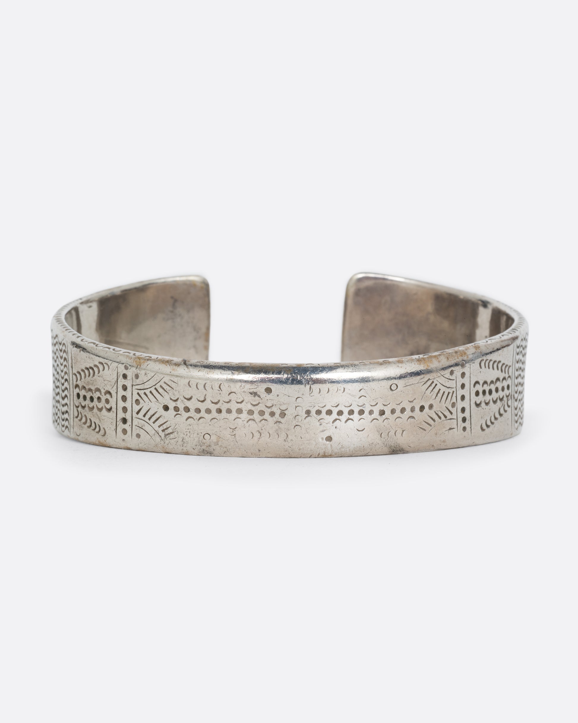 A silver bracelet with a graduated silhouette, hand stamped pattern, and opening in the front. Shown from the back.