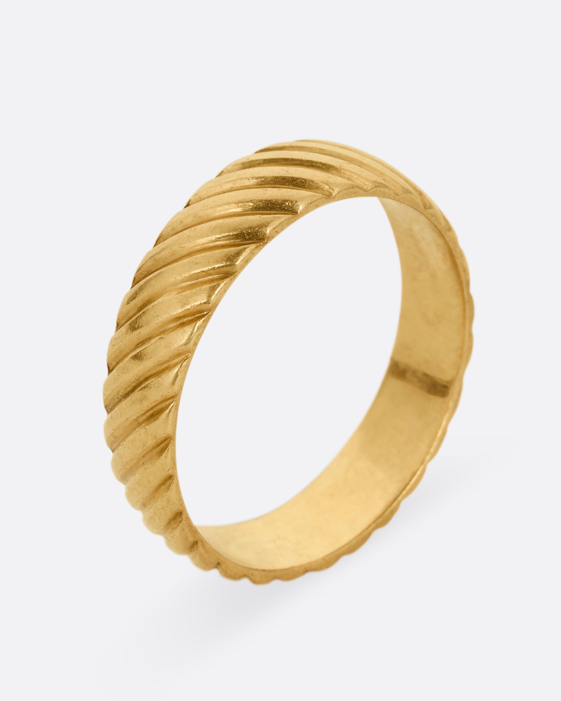 A wide yellow gold ring with an all over diagonal linear pattern. Shown standing up from the side.