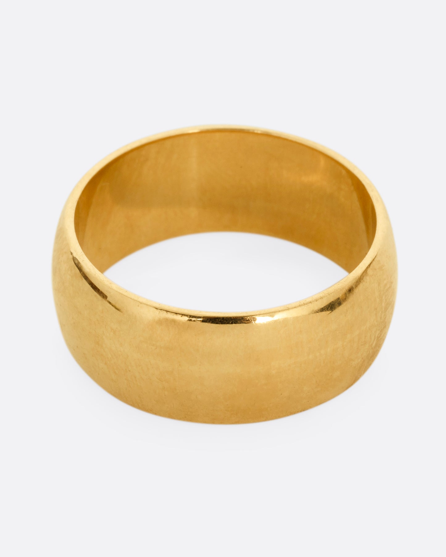 A broad yellow gold band with a rounded silhouette. Shown from the top. 