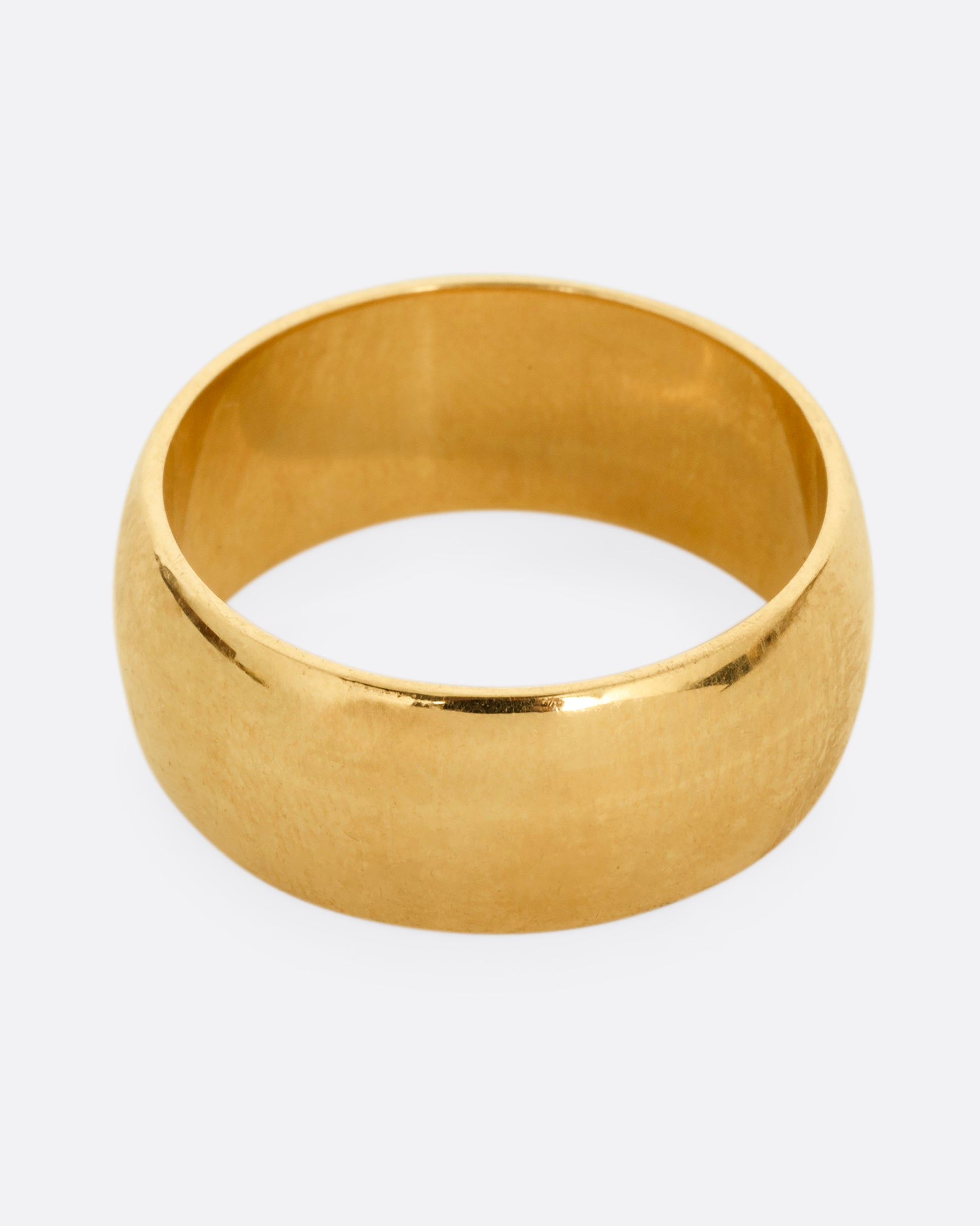 A broad yellow gold band with a rounded silhouette. Shown from the top. 
