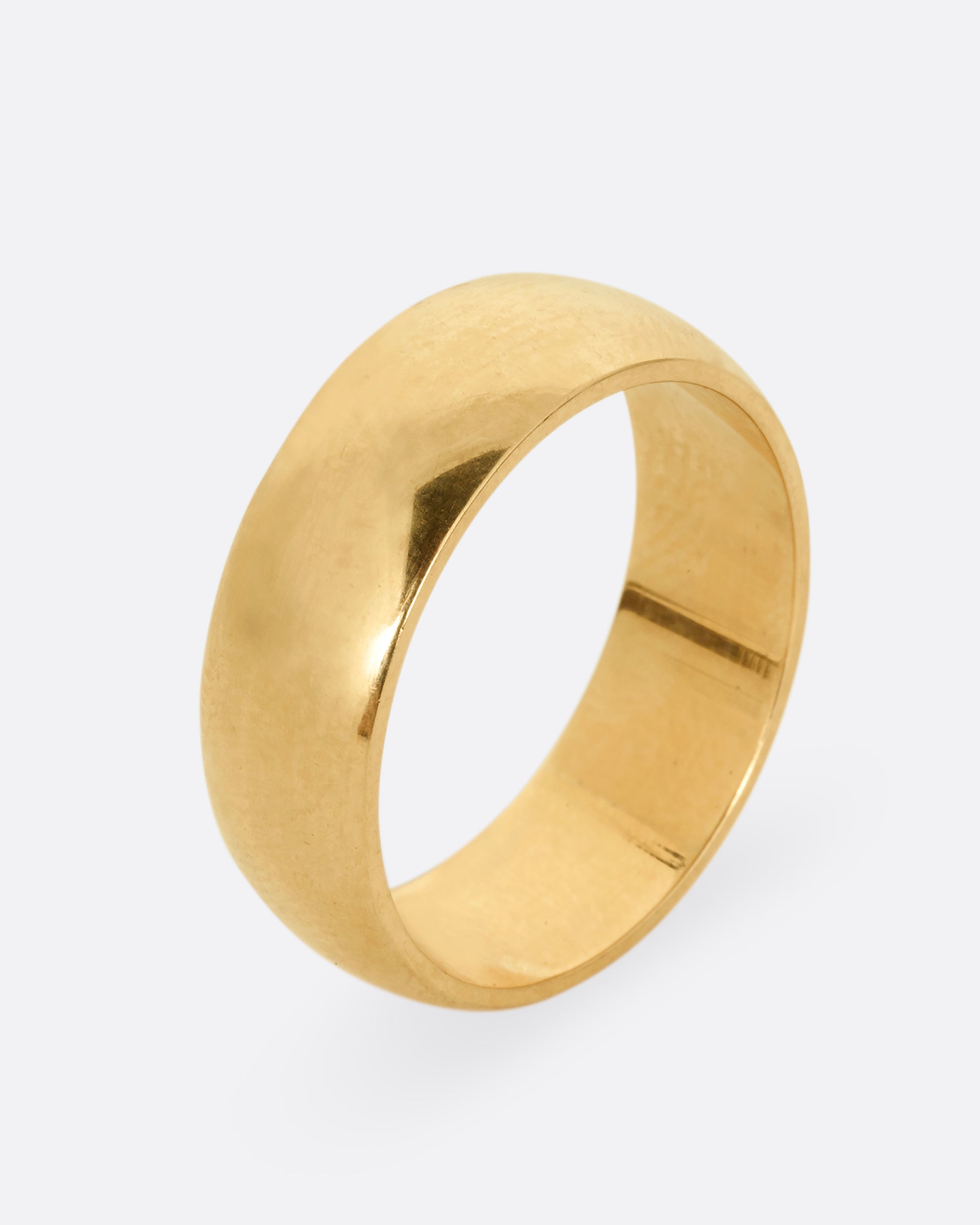 A broad yellow gold band with a rounded silhouette. Shown standing up from the side. 