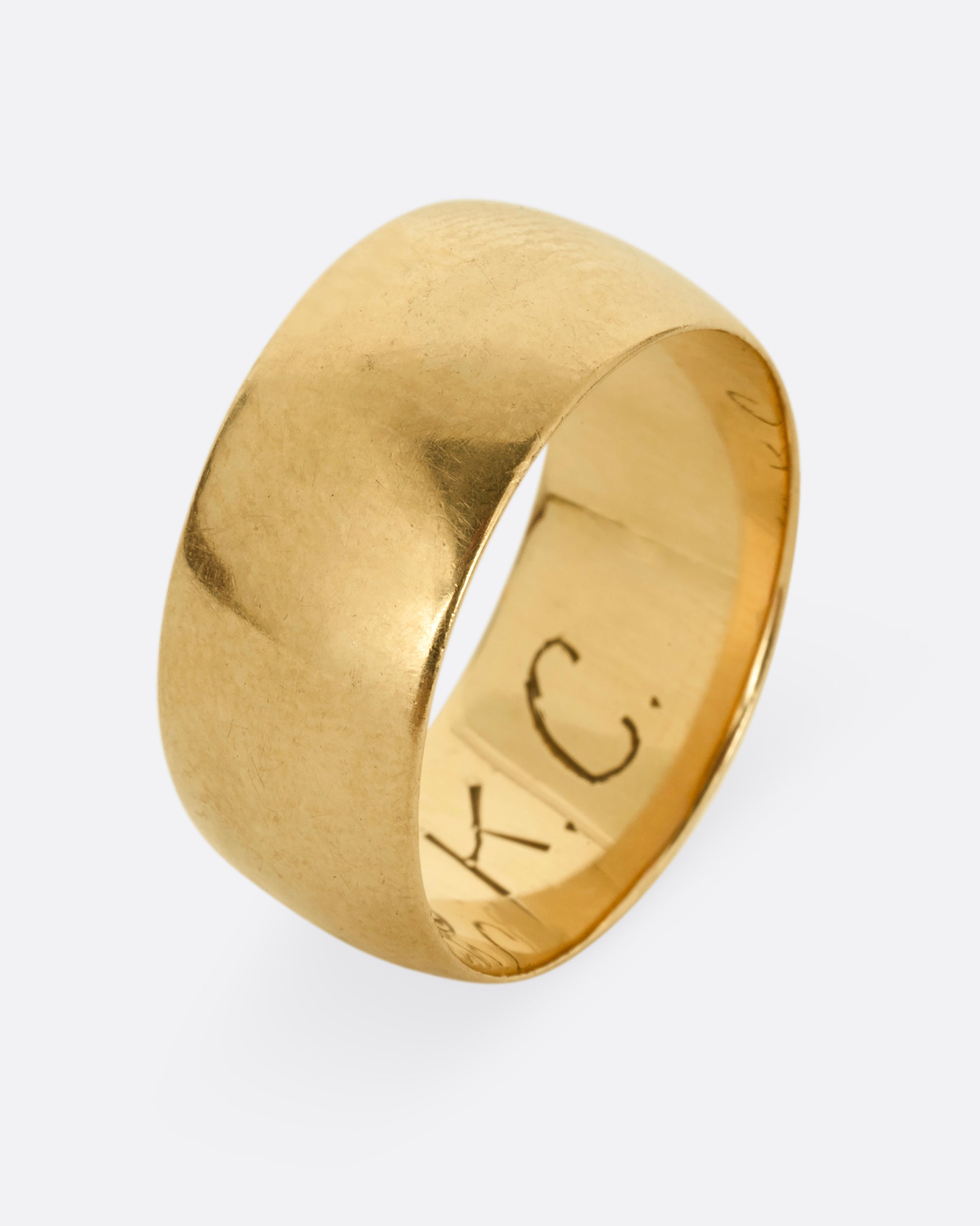 A thick yellow gold cigar band with T.C. to K engraved on the inside. Shown standing up from the side.