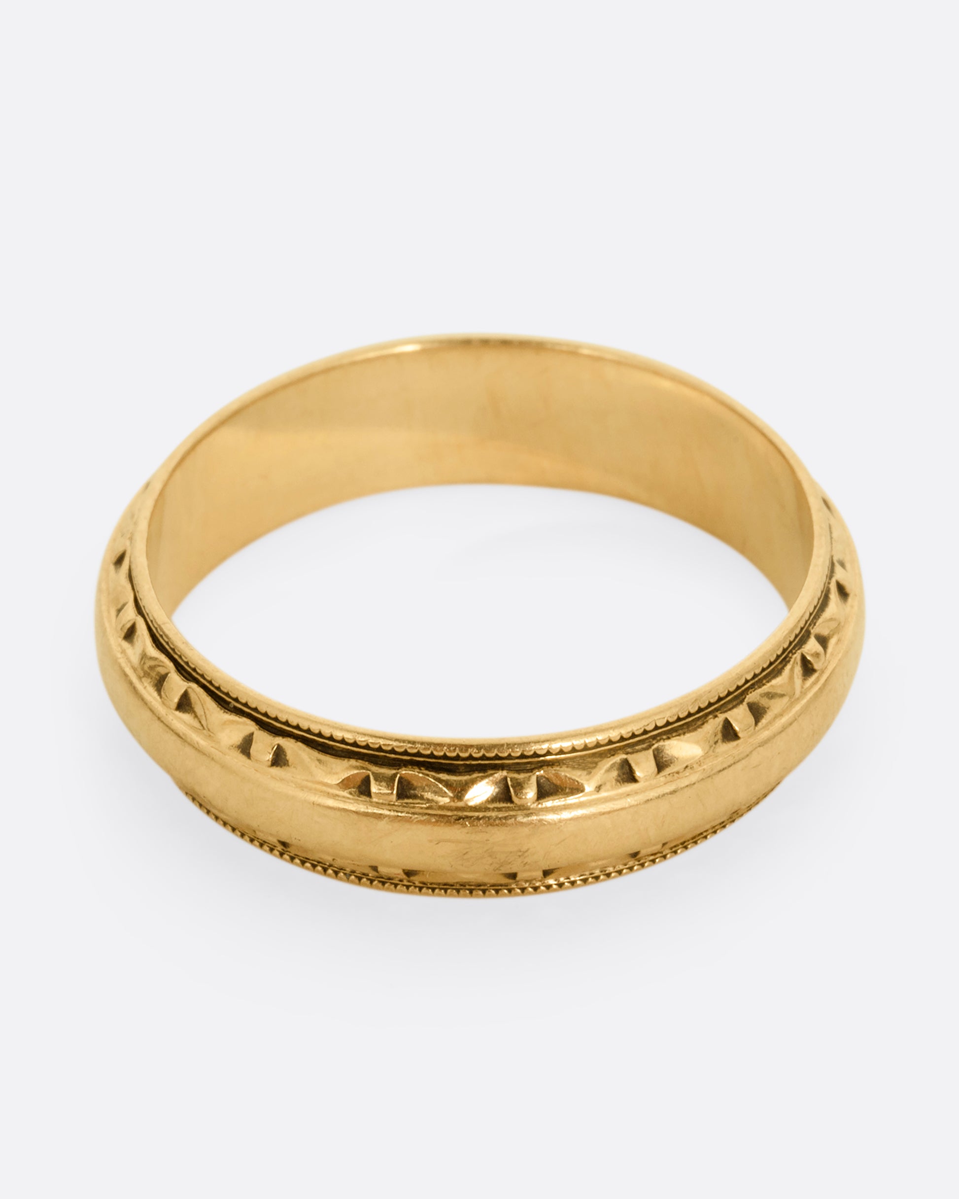 A yellow gold ring with a subtle geometric pattern on its edges. Shown from the front.