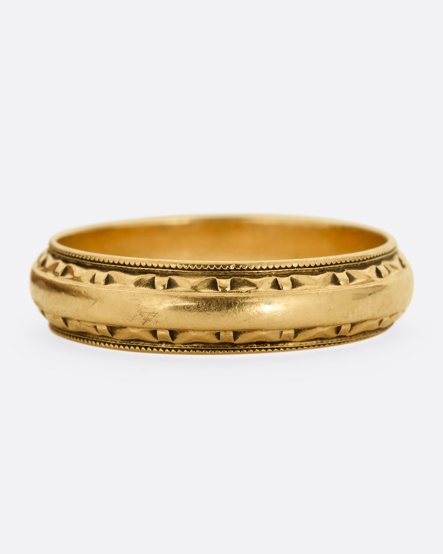 A yellow gold ring with a subtle geometric pattern on its edges. Shown from the front.