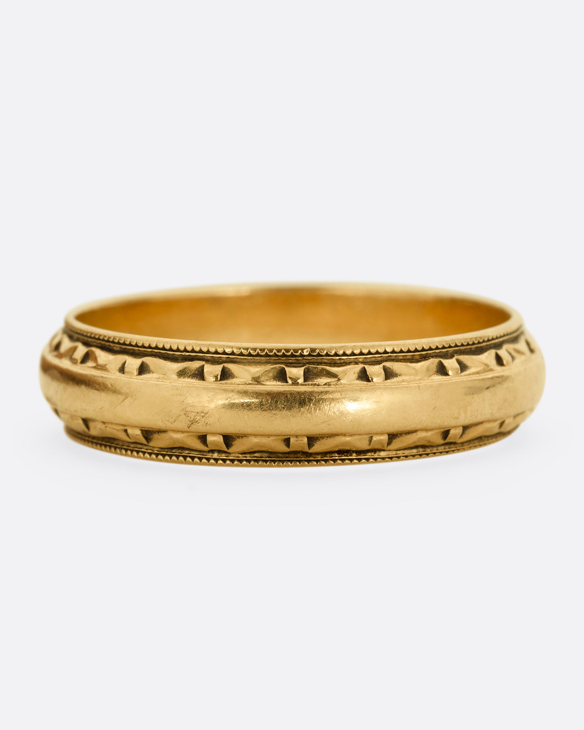 A yellow gold ring with a subtle geometric pattern on its edges. Shown from the front.