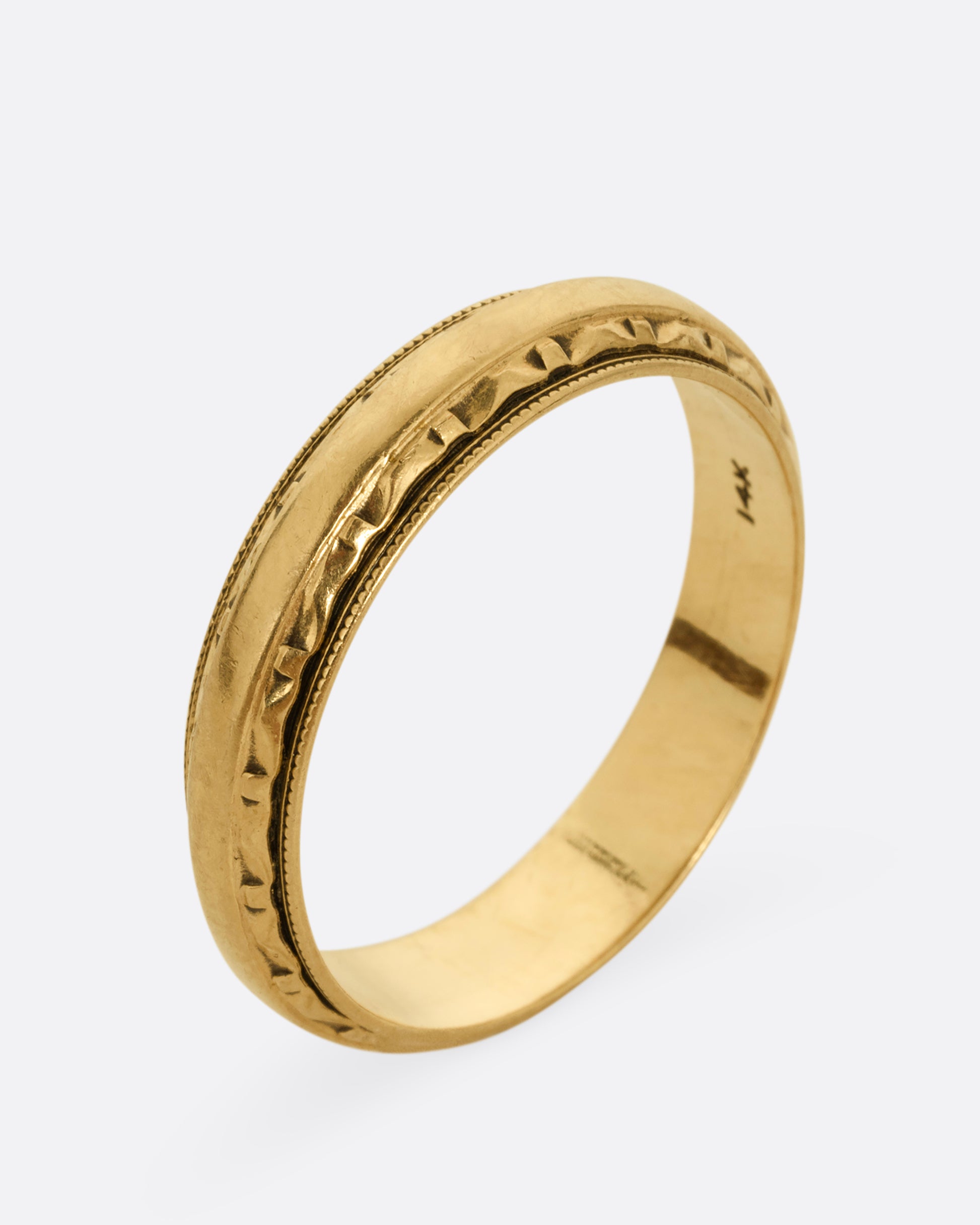 A yellow gold ring with a subtle geometric pattern on its edges. Shown standing up from the side.