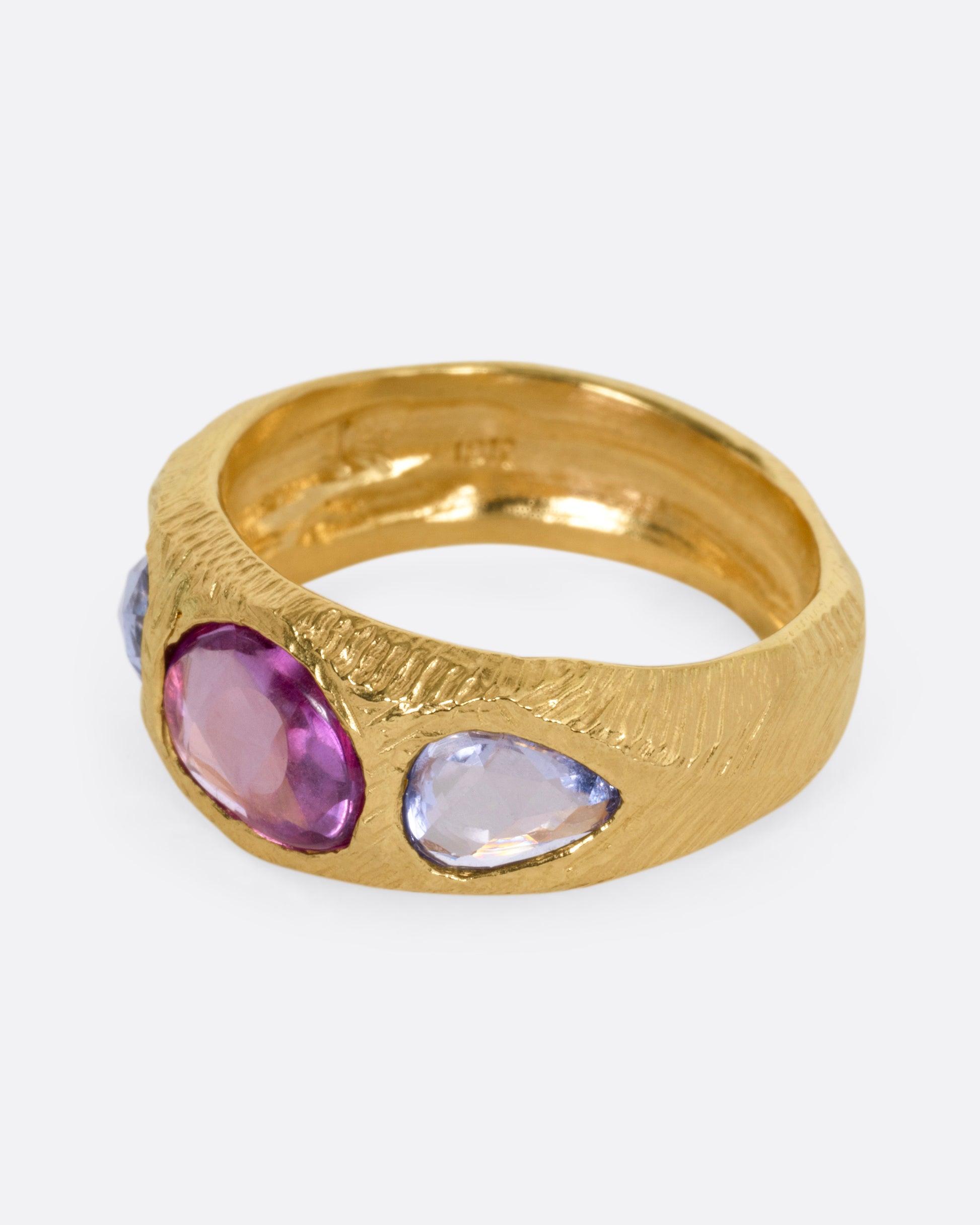 A yellow gold ring with two blue sapphires and one pink, shown from the side.