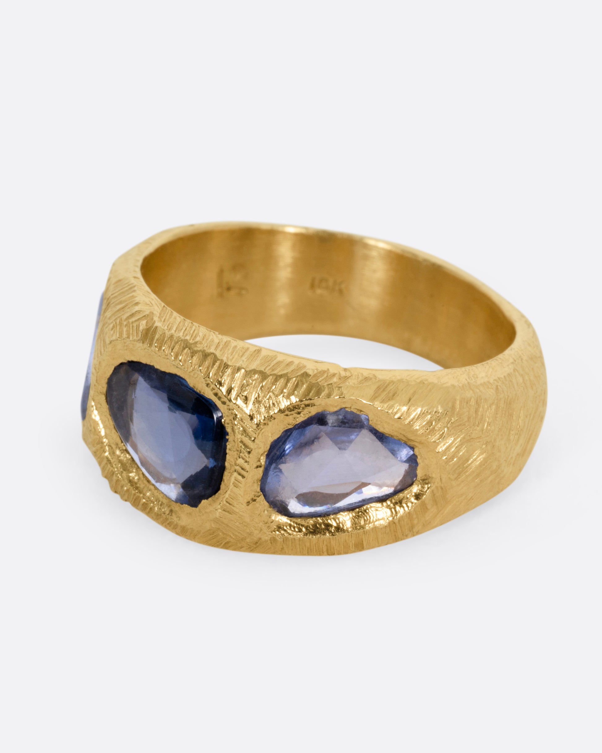 A yellow gold ring with three blue sapphires, shown from the side.