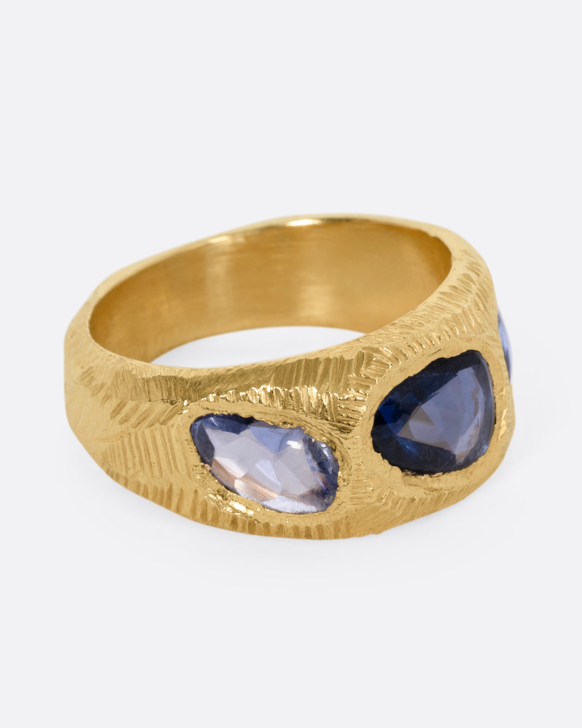 A yellow gold ring with three blue sapphires, shown from the side.