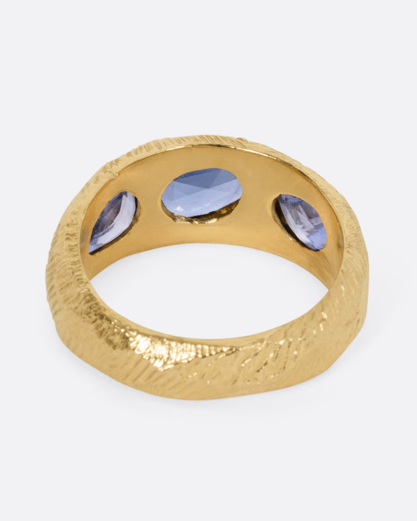 A yellow gold ring with three blue sapphires, shown from the back.