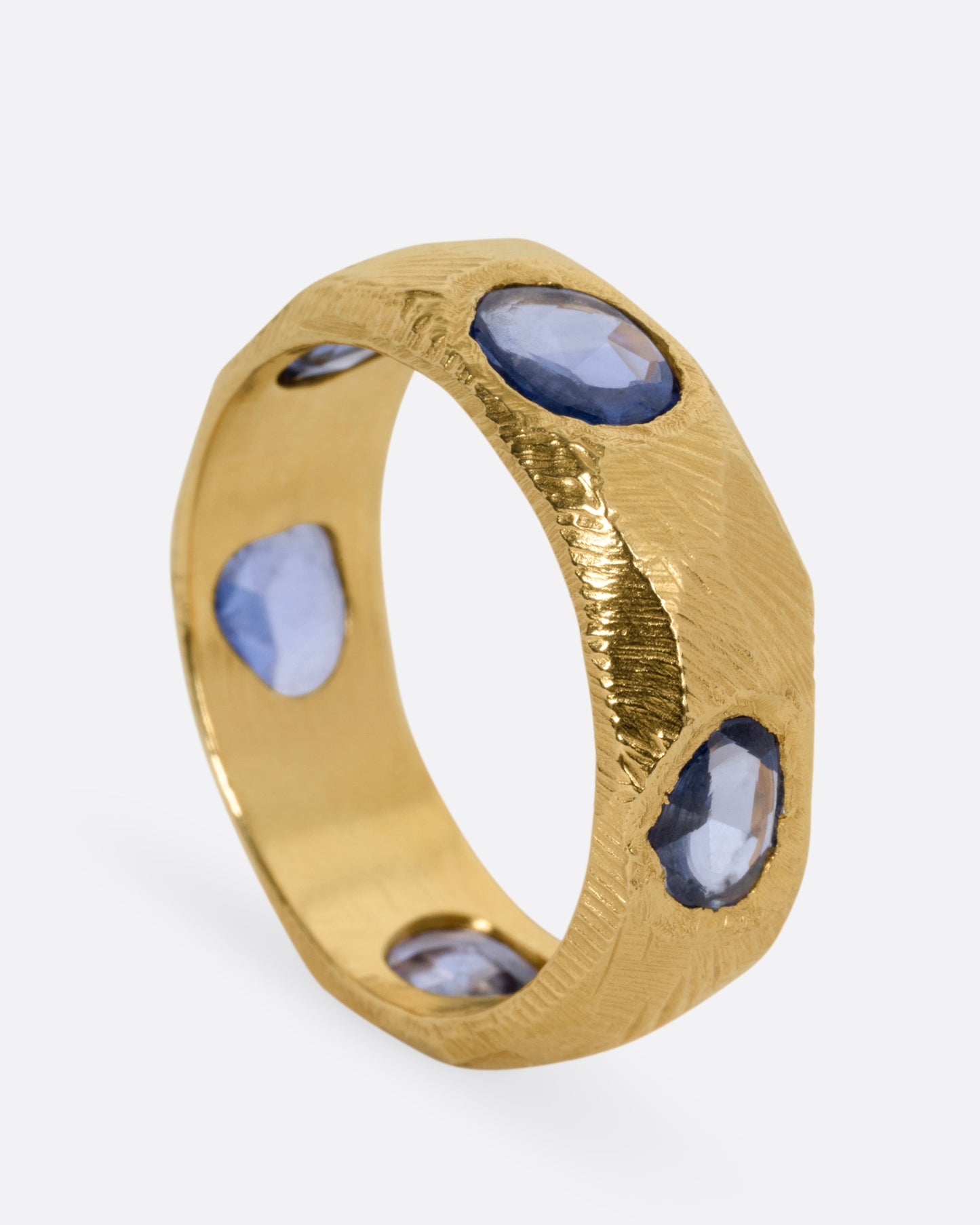 A yellow gold ring with five blue sapphires, shown standing up from the side.