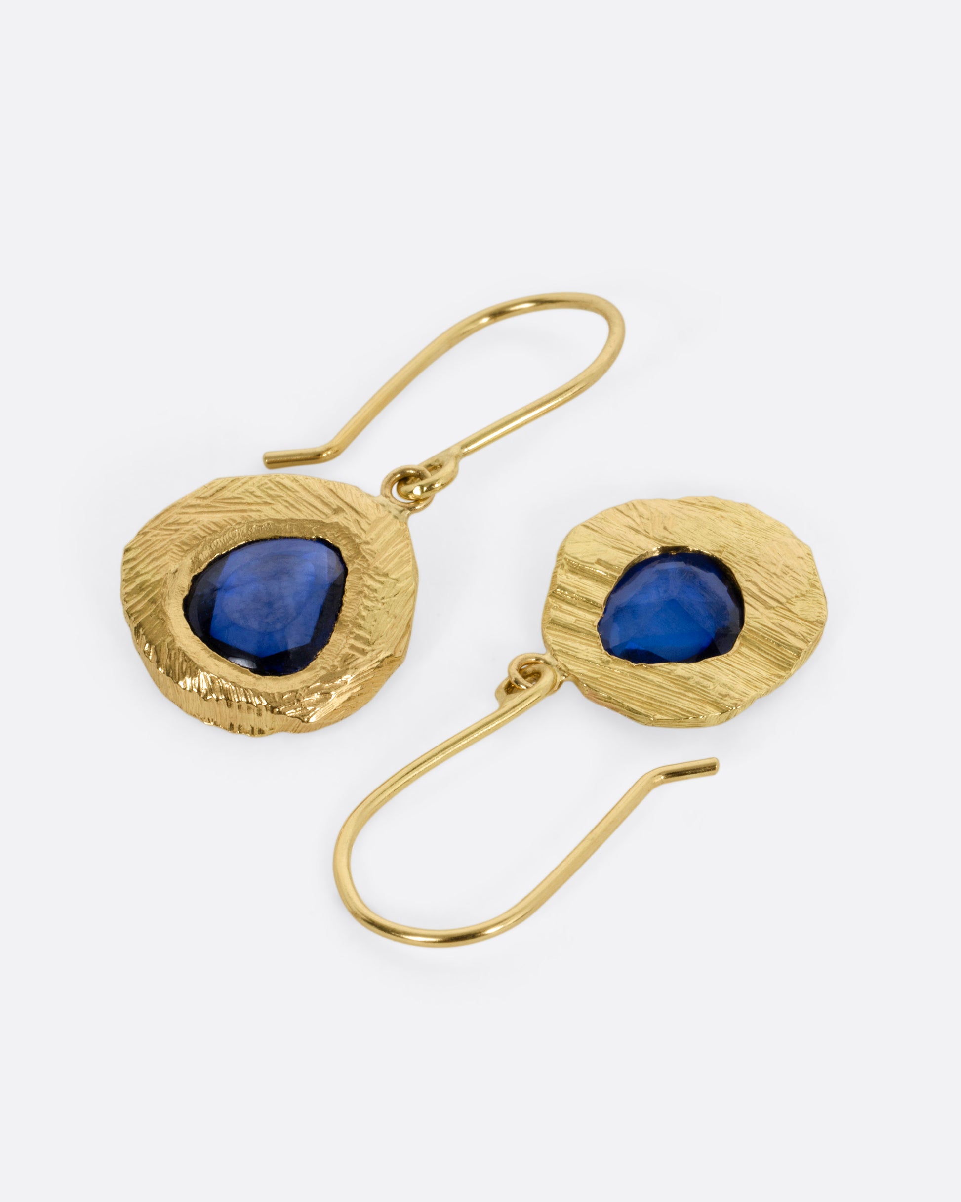 A pair of yellow gold drop earrings with blue sapphires. One earring is shown from the front, the other from the back.