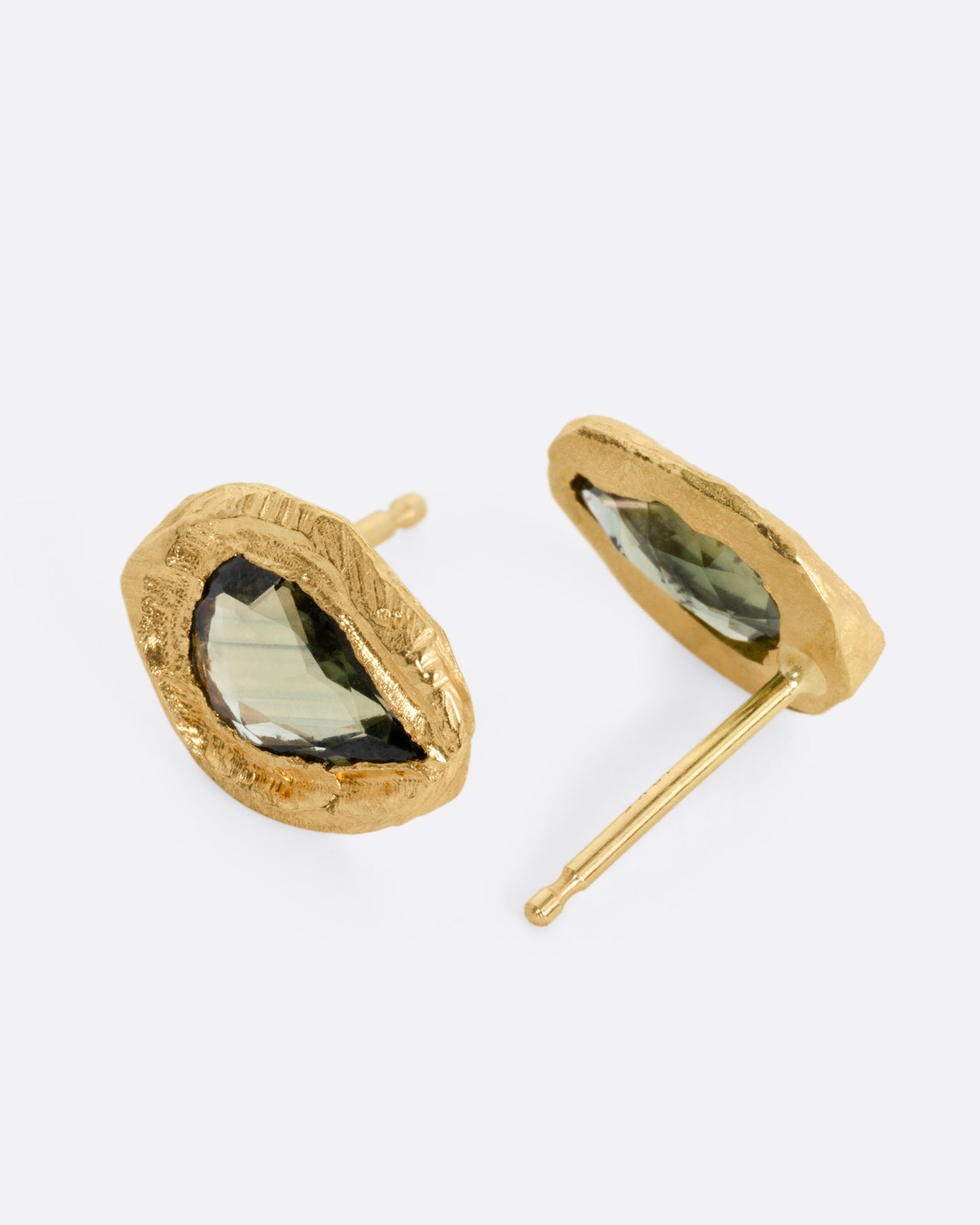 A pair of yellow gold stud earrings with teardrop shaped green sapphires, shown on their sides.