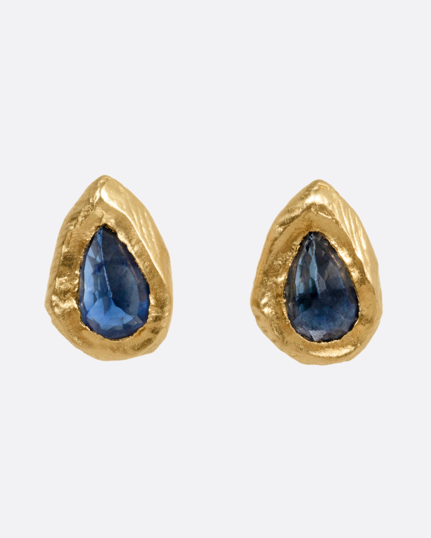 A pair of yellow gold stud earrings with teardrop shaped blue sapphires, shown from the front.