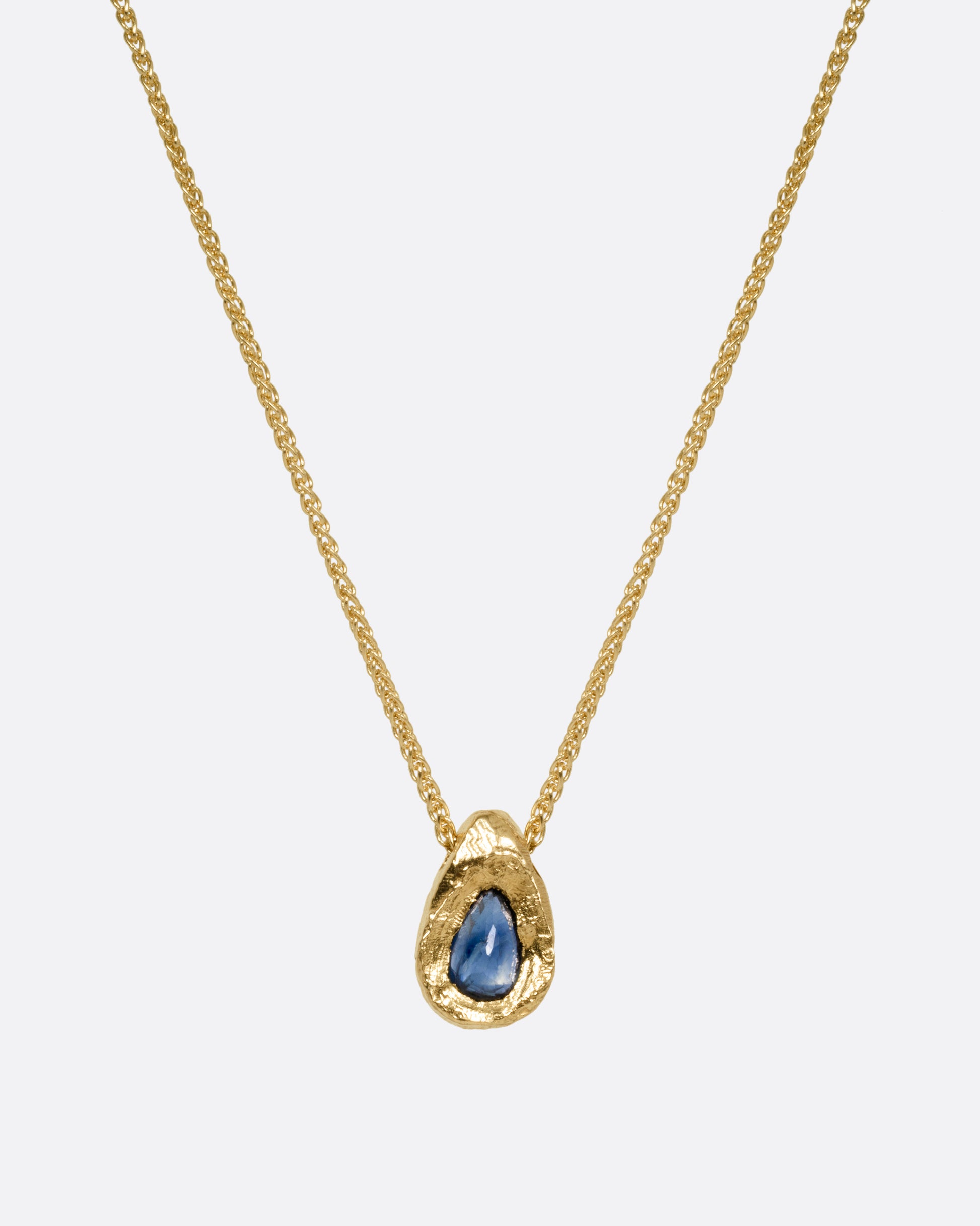 A yellow gold necklace with a blue sapphire pendant shown from the front.