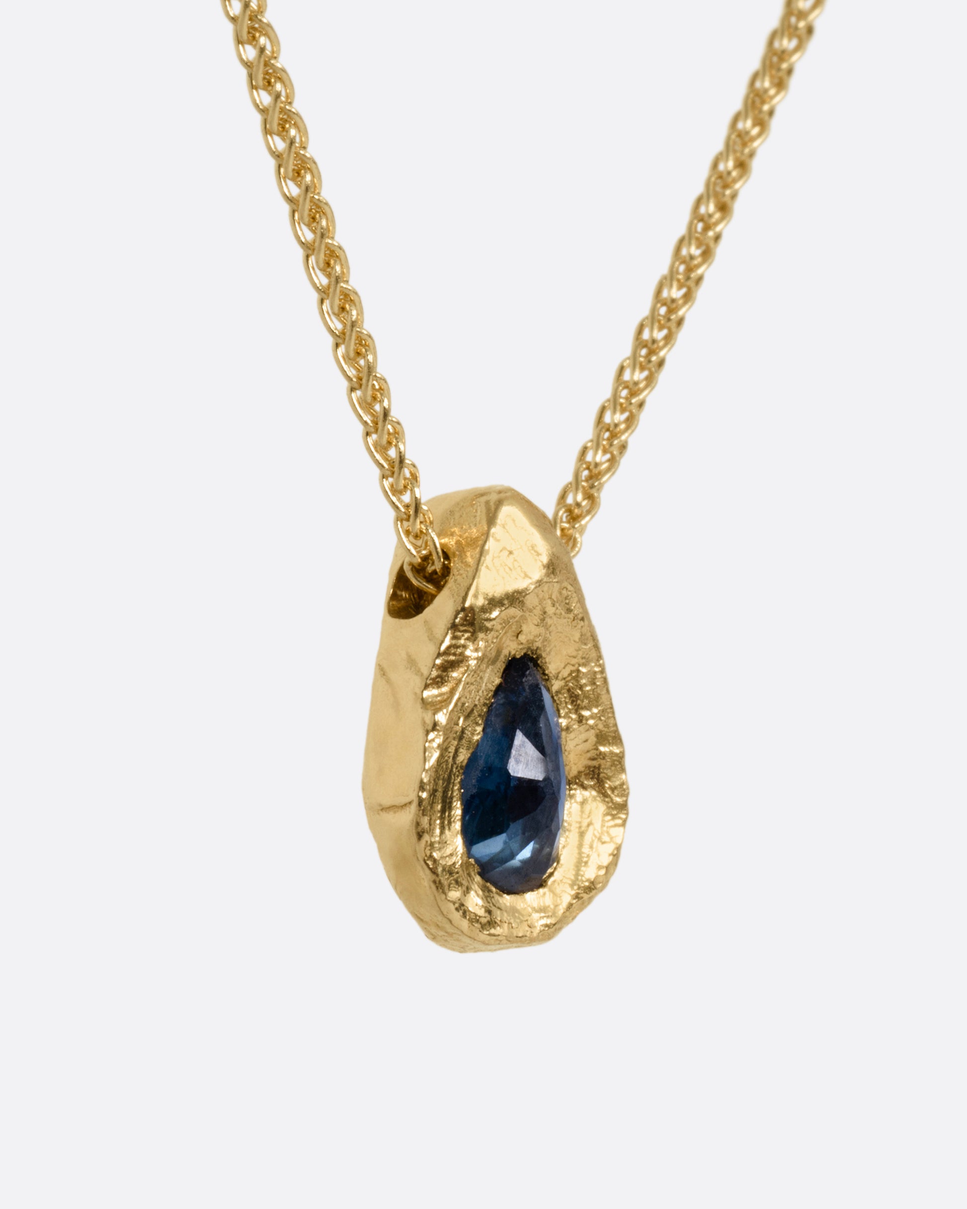 A yellow gold necklace with a blue sapphire pendant shown from the side.