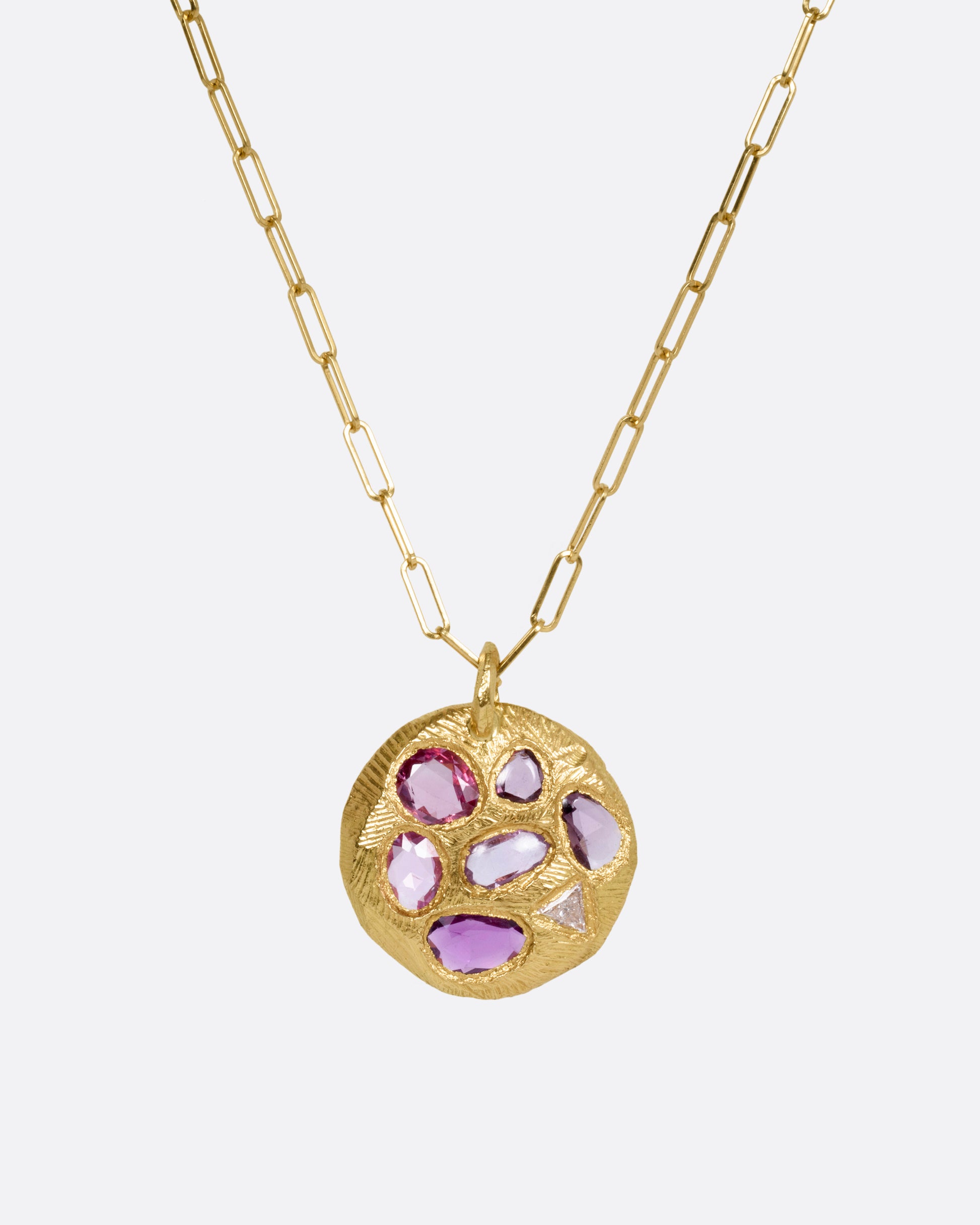A yellow gold necklace with a circular pendant with pink sapphires and one trillion cut diamond, shown from the front.